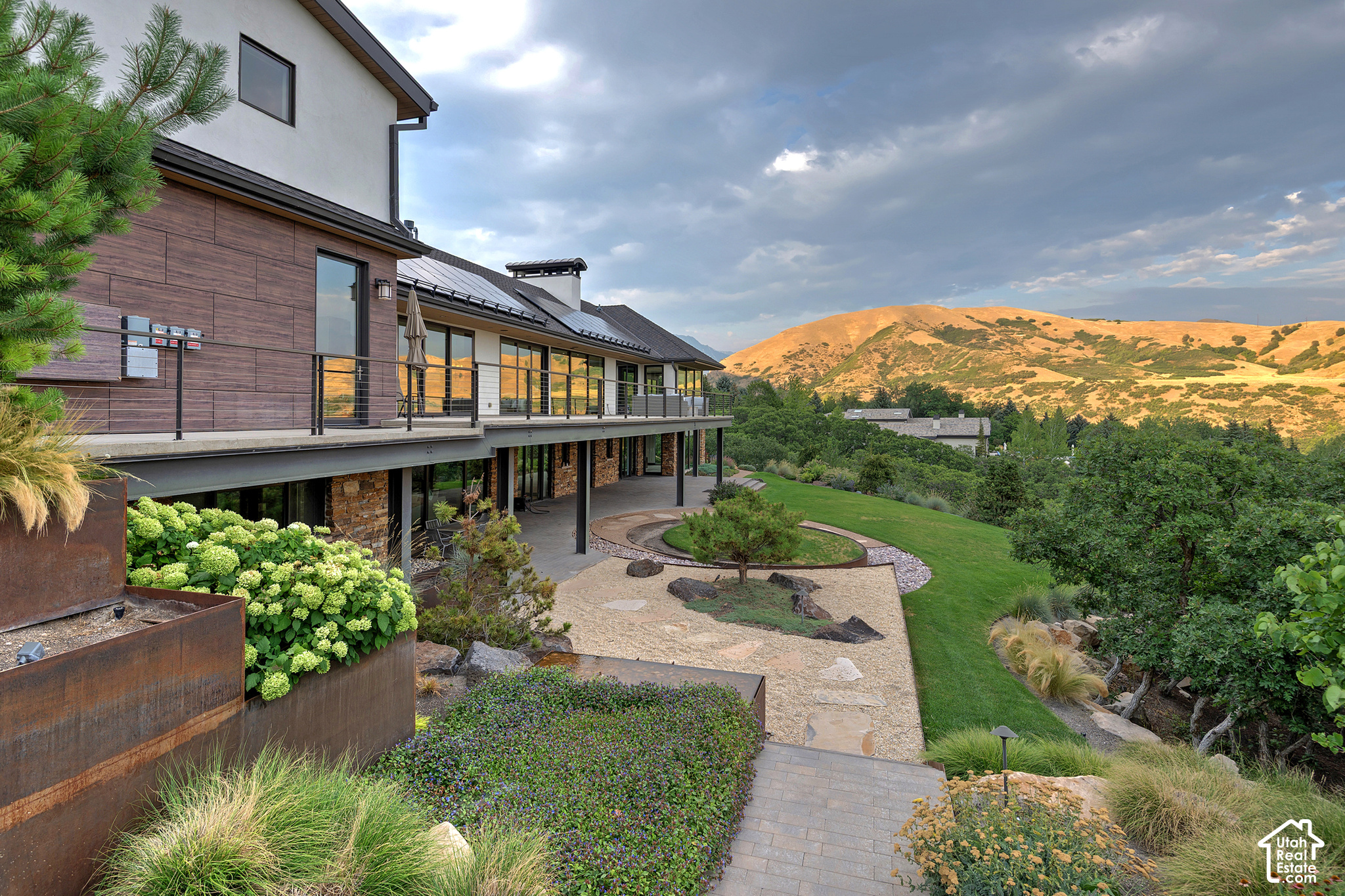 Modern wood-and-stone home with a landscaped yard and sunlit golden hills beyond.