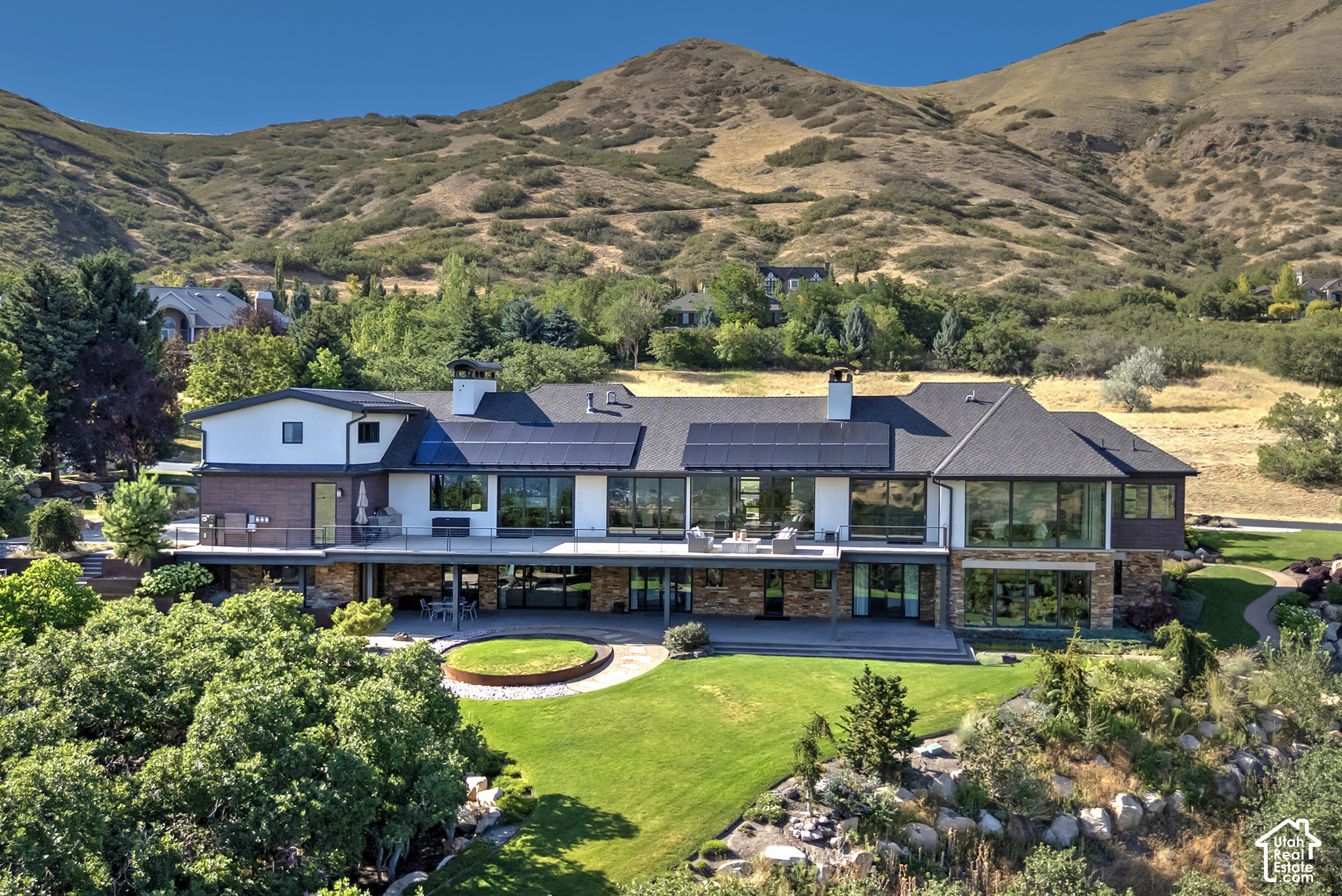 Modern home with rooftop solar panels, landscaped lawn, and mountain backdrop.