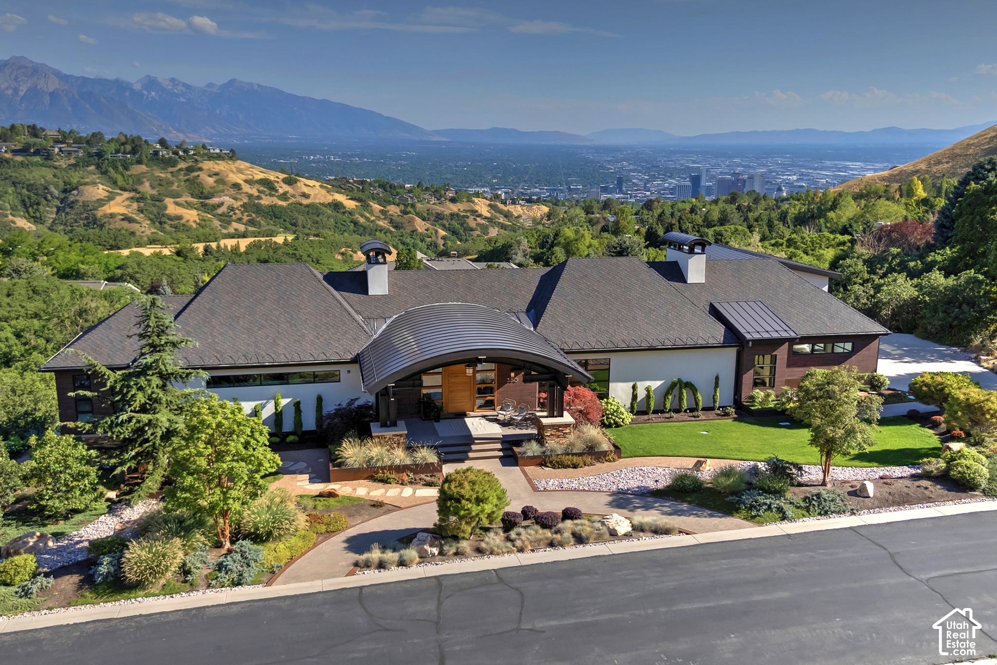 Aerial view of a modern home with curved entry canopy, landscaped yard, and mountain-valley backdrop.