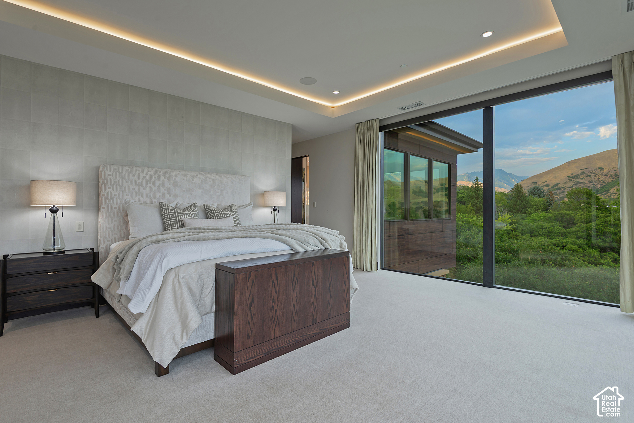 Modern bedroom with a king bed and floor-to-ceiling windows overlooking green trees and mountains.