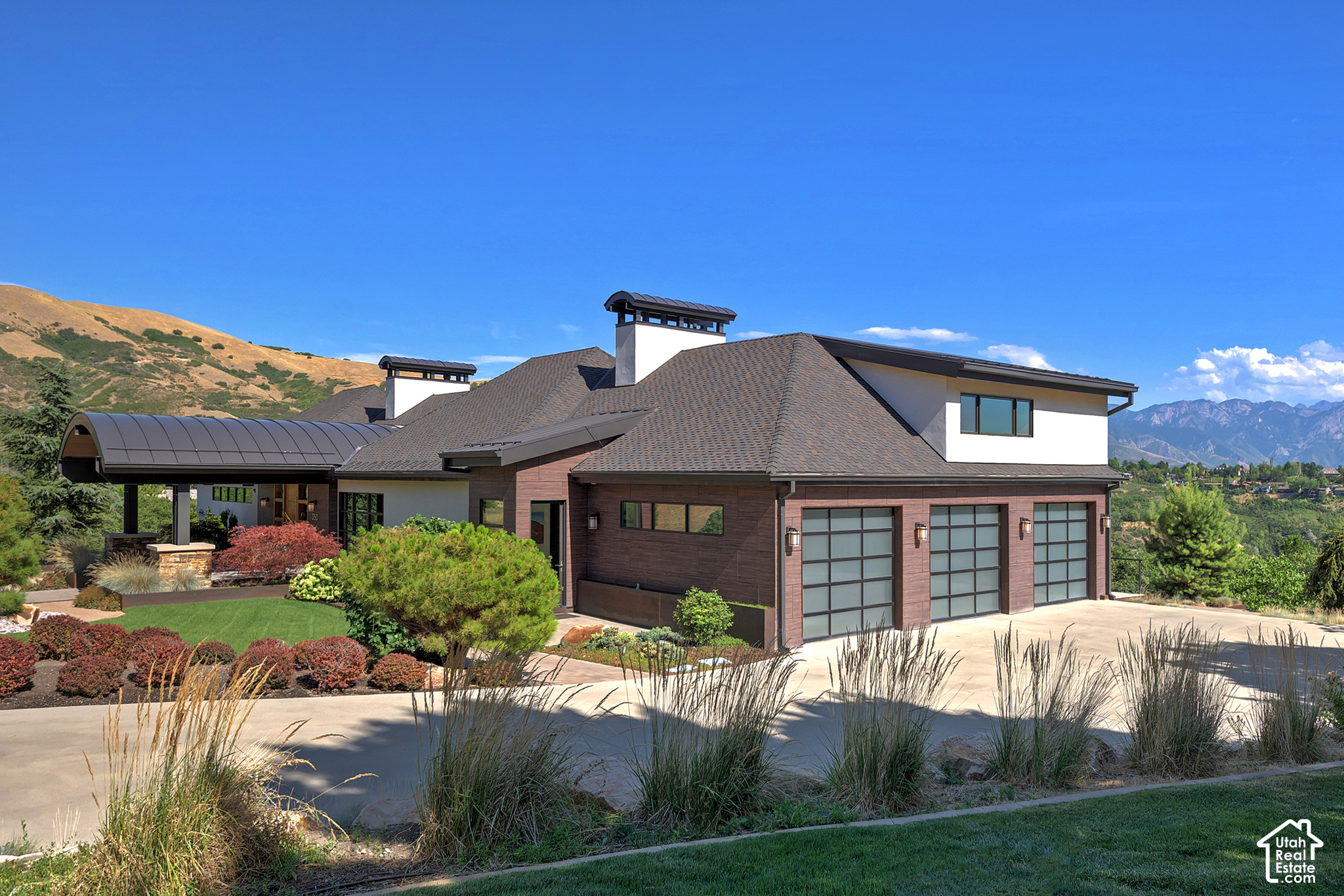 Contemporary home with three glass-paneled garage doors, landscaped yard, and mountains behind it.