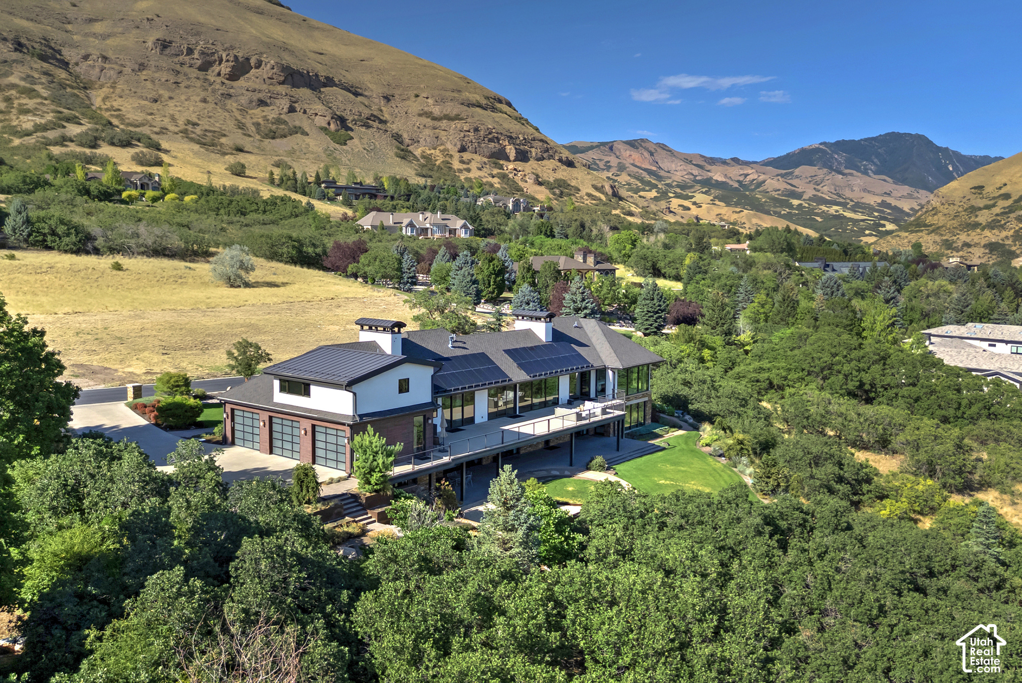 Modern home with solar panels and a long deck, surrounded by trees with mountains behind it.