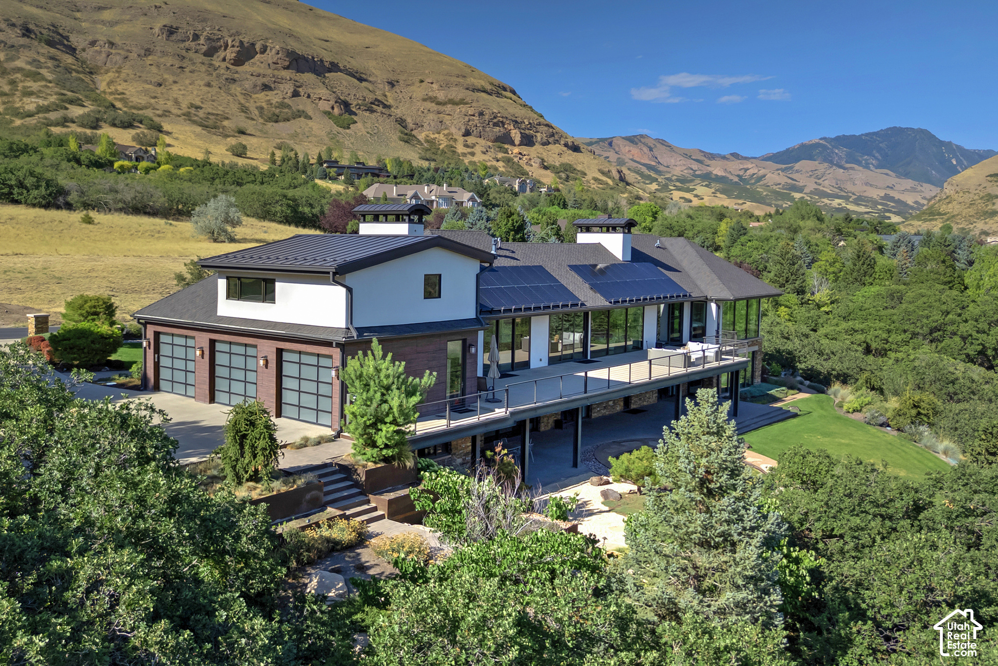 Modern home with solar panels and a long deck, surrounded by landscaped grounds and mountain views.