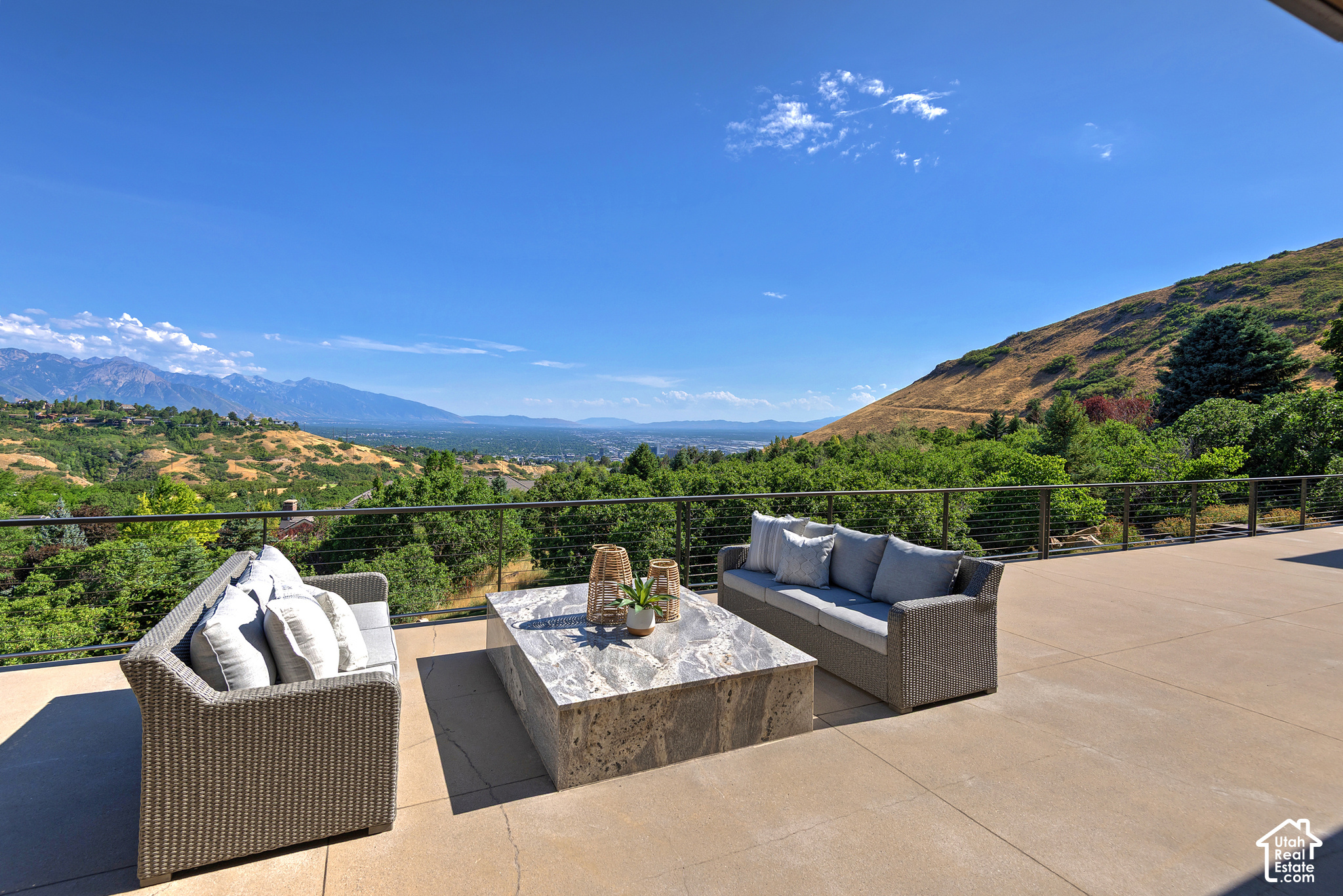 Furnished patio with wicker seating overlooking a valley and distant mountains.