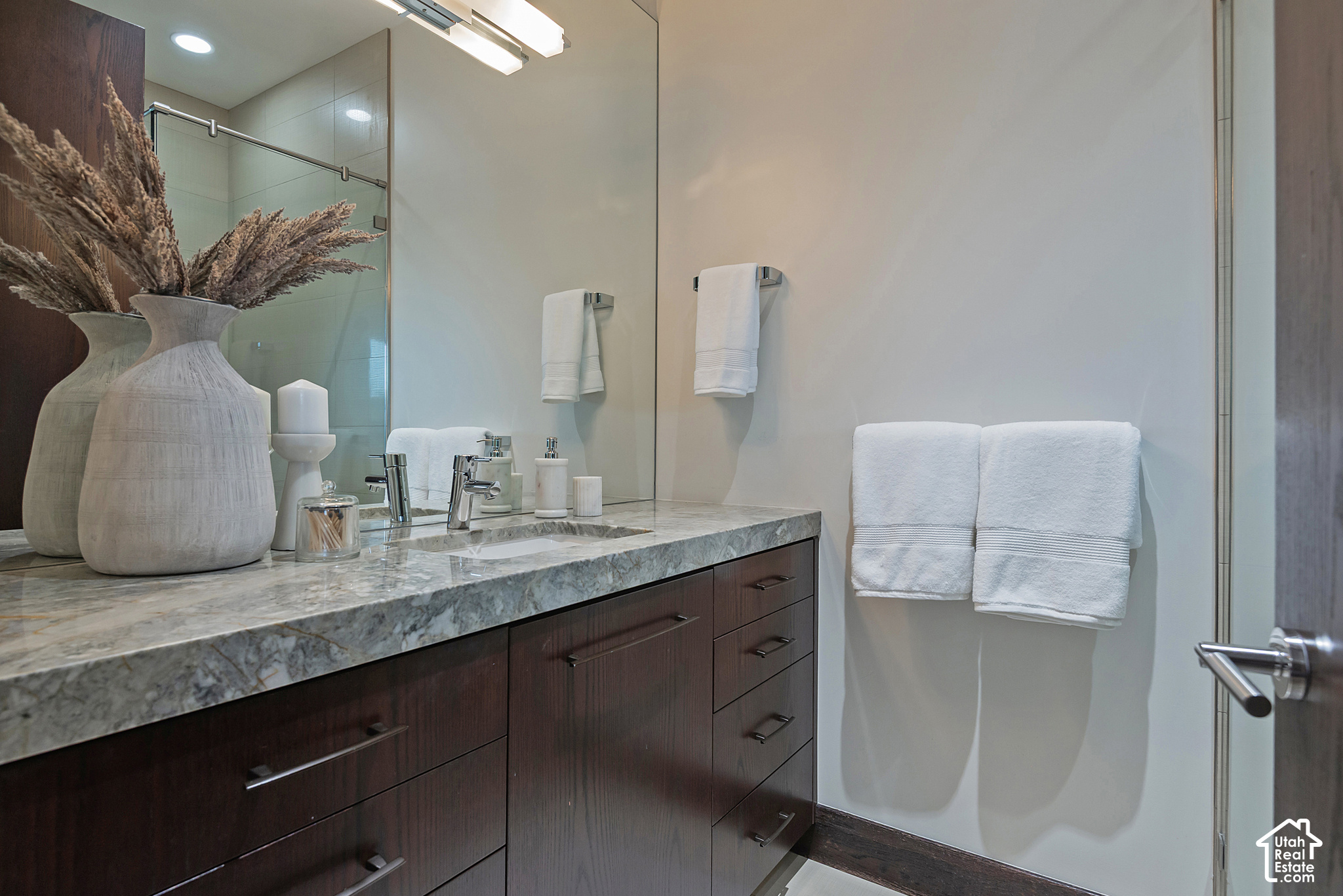Modern bathroom vanity with a veined stone countertop, large mirror, and glass shower.