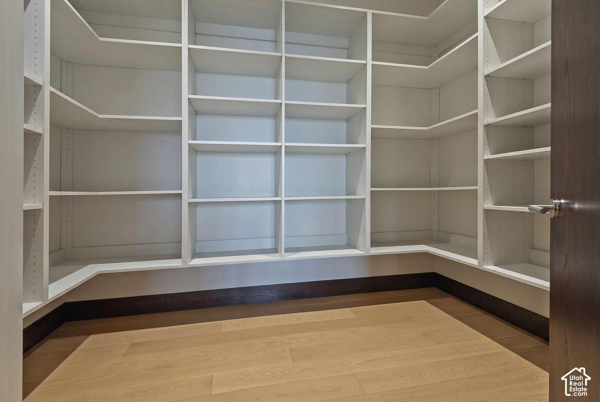 Walk-in closet with wraparound white shelving and light wood floors.