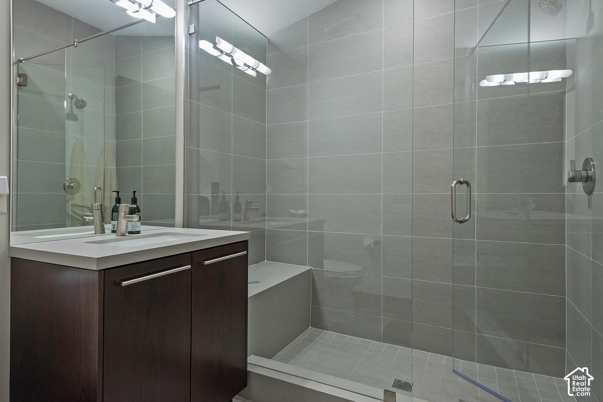 Bathroom with a dark wood vanity and spacious gray-tiled glass walk-in shower.