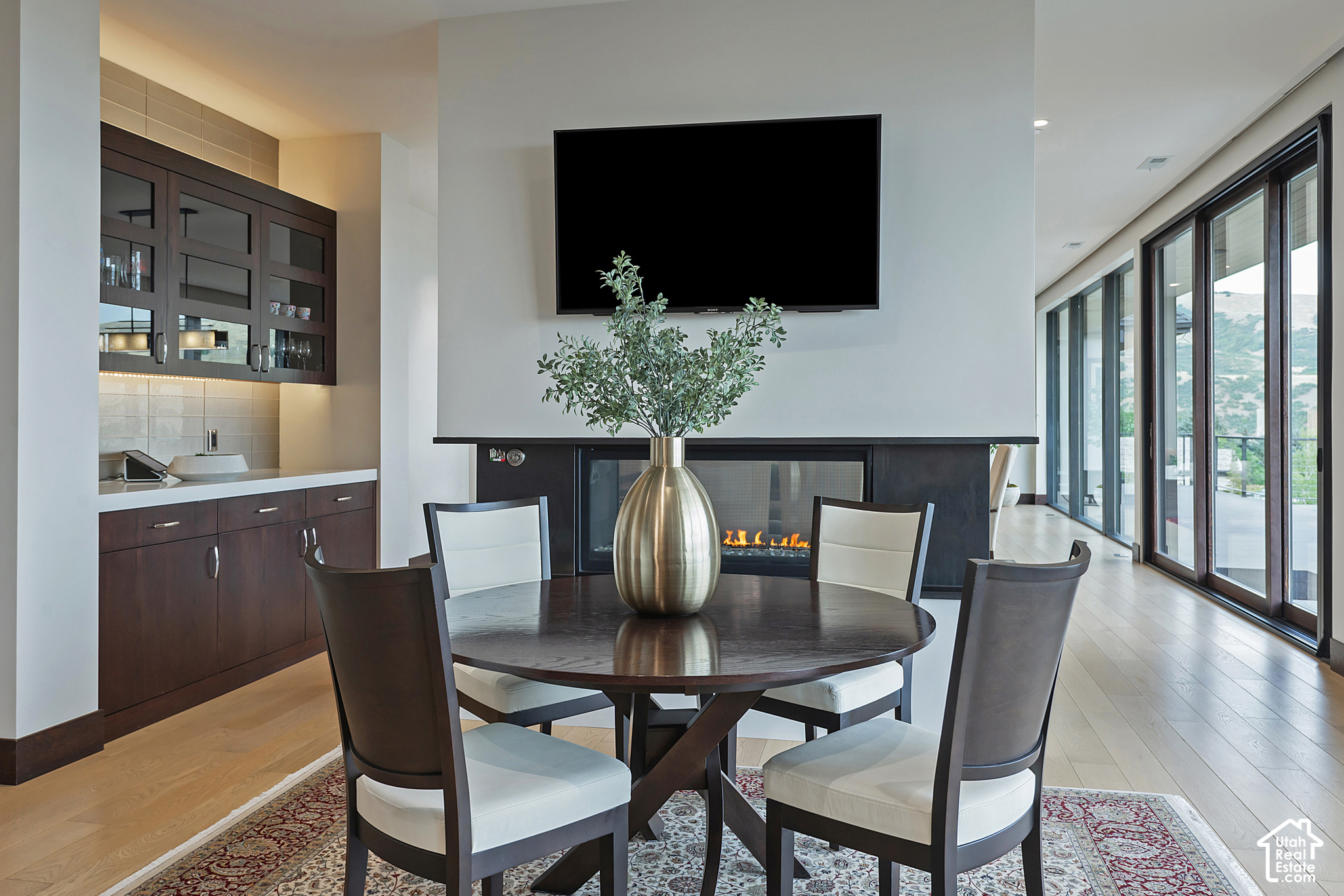 Dining area with a round table, built-in cabinetry, linear fireplace, and tall glass doors overlooking distant hills.
