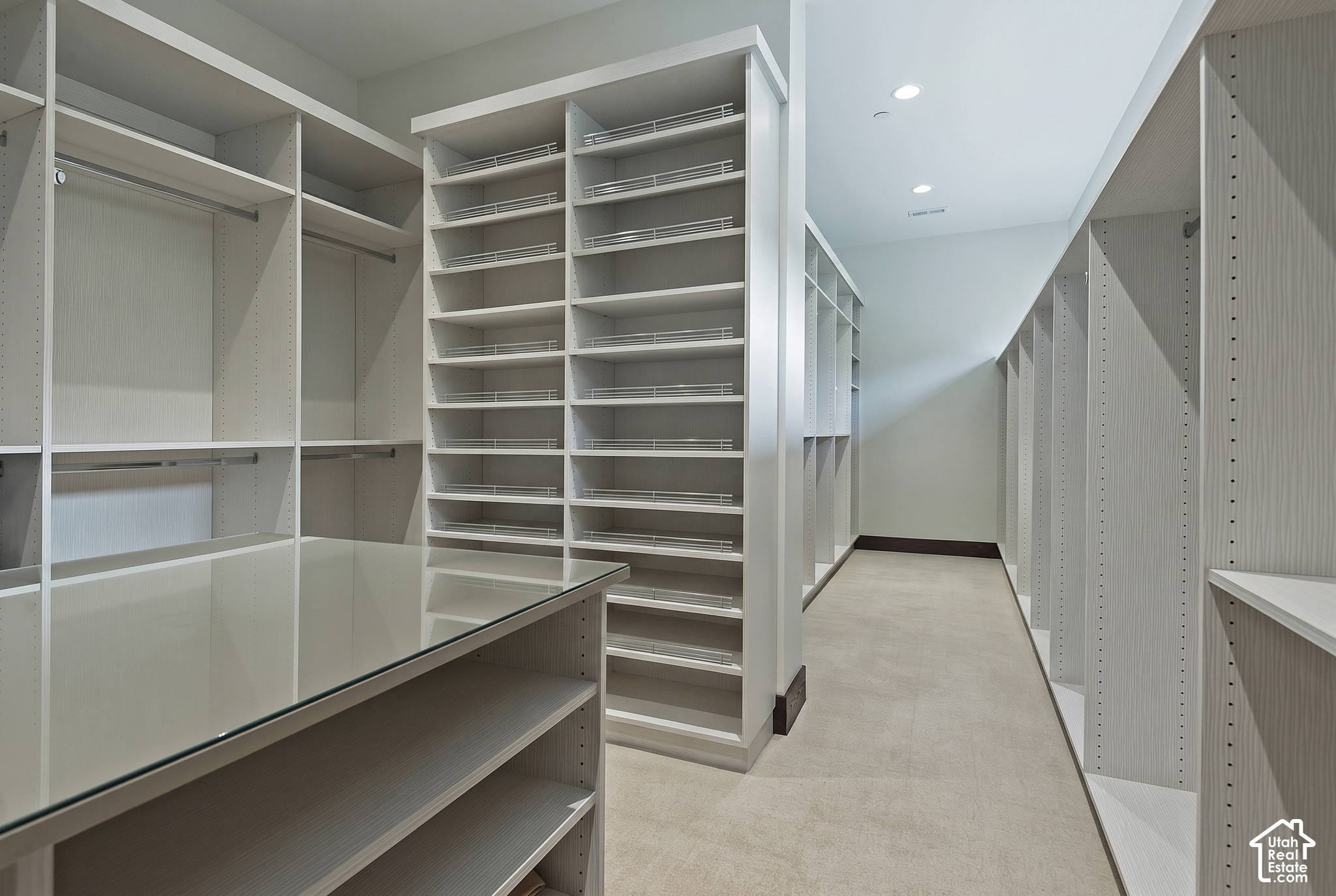 Walk-in closet with extensive white built-in shelving and a glass-topped central island.