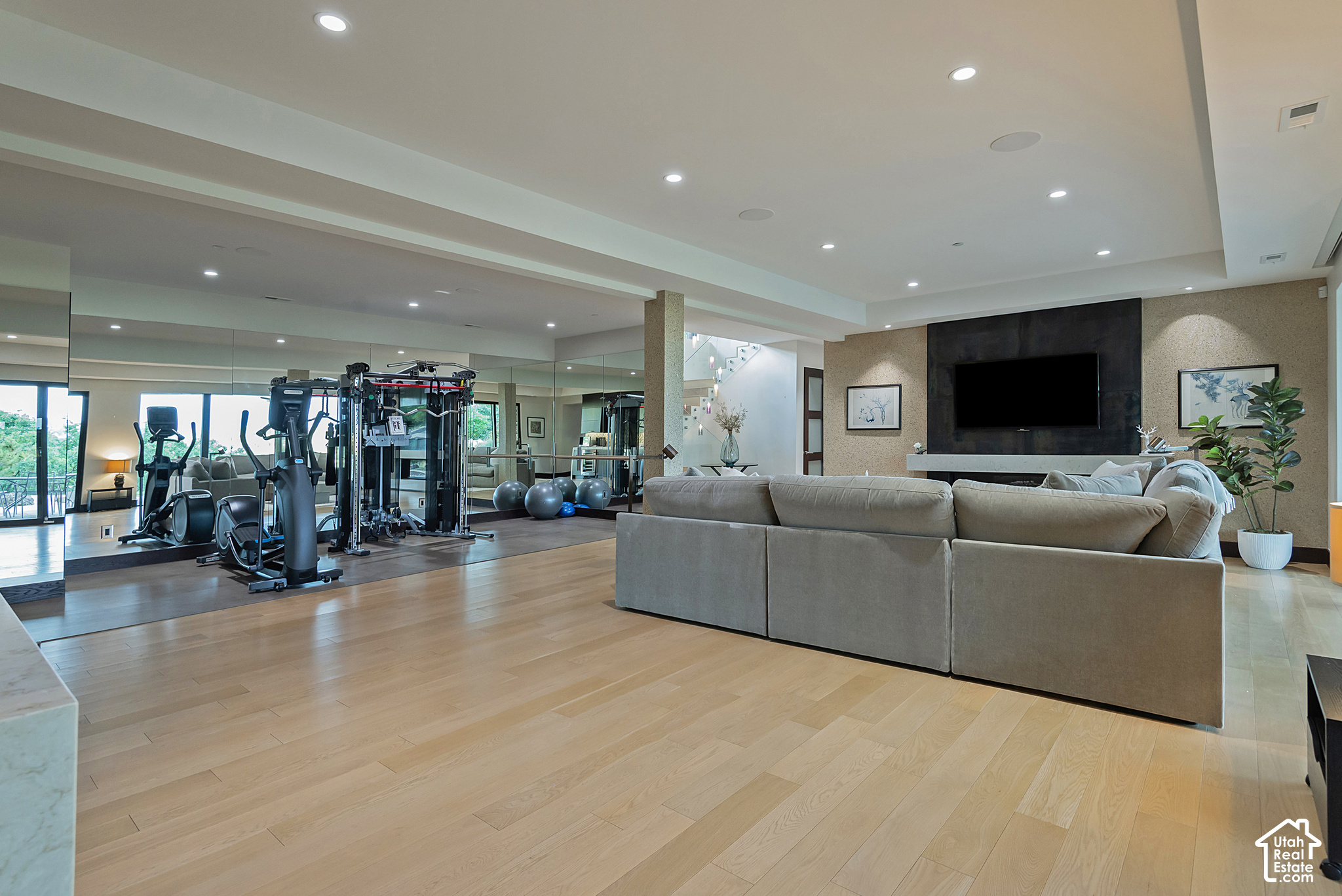 Modern living room with a large sectional sofa beside a mirrored home gym.