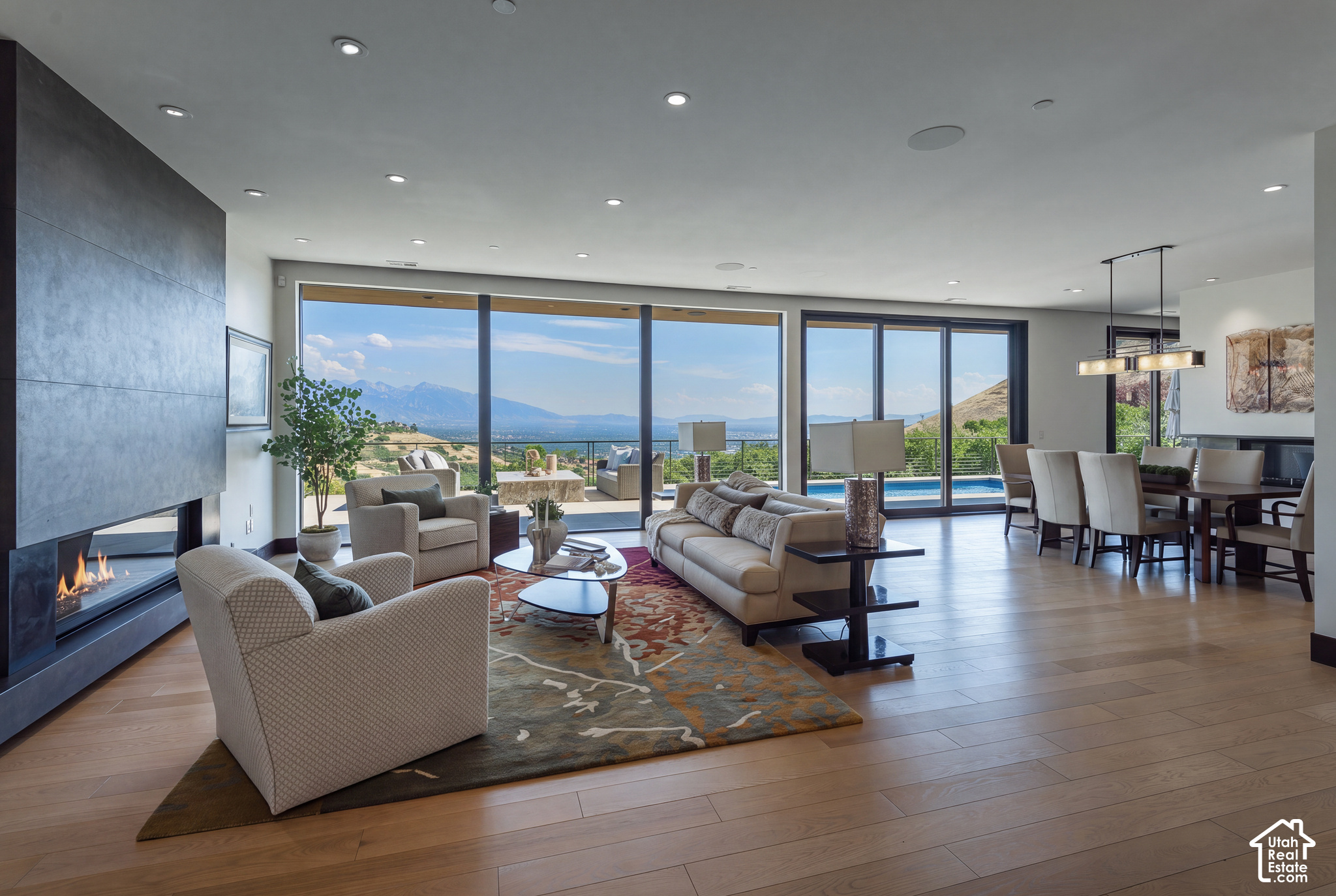 Open-plan living and dining room with a modern fireplace, mountain views, and windows overlooking a poolside patio.