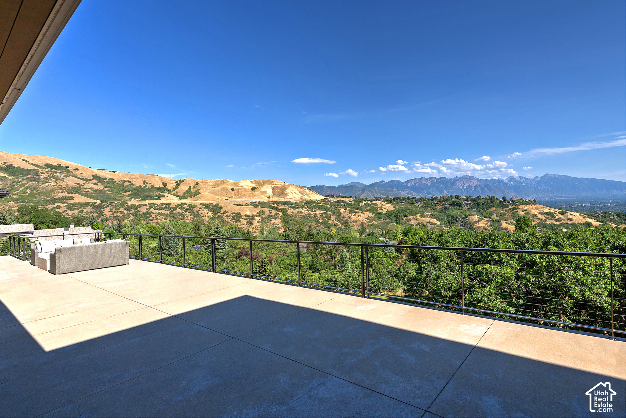 Terrace with cushioned seating overlooking green foothills and distant mountains.