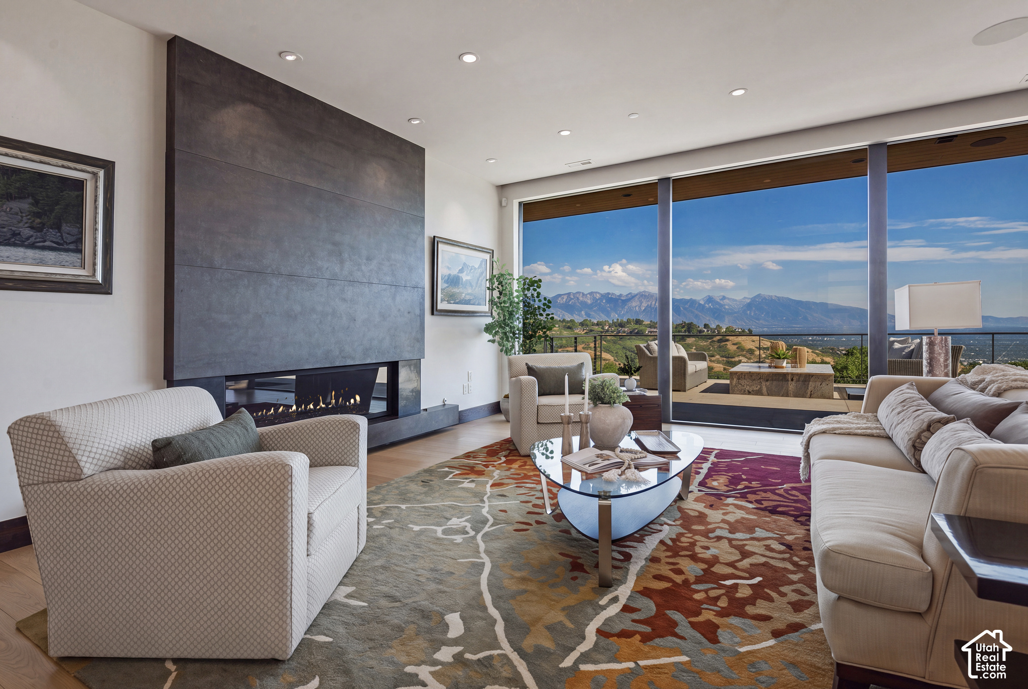 Staged living room with a stone fireplace and mountain views through floor-to-ceiling windows.