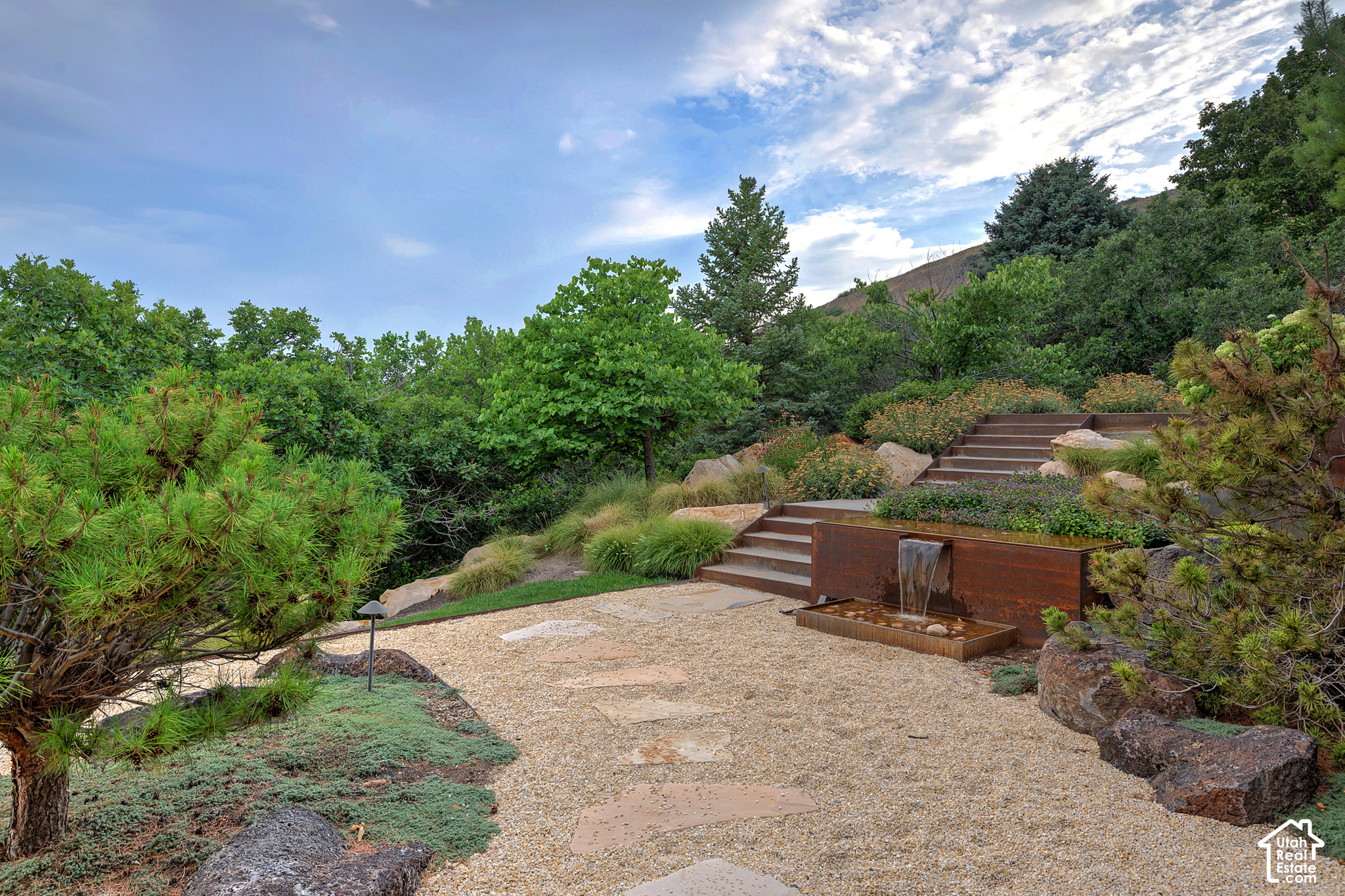 Landscaped garden with gravel paths, tiered stone steps, and a rust-colored waterfall feature.