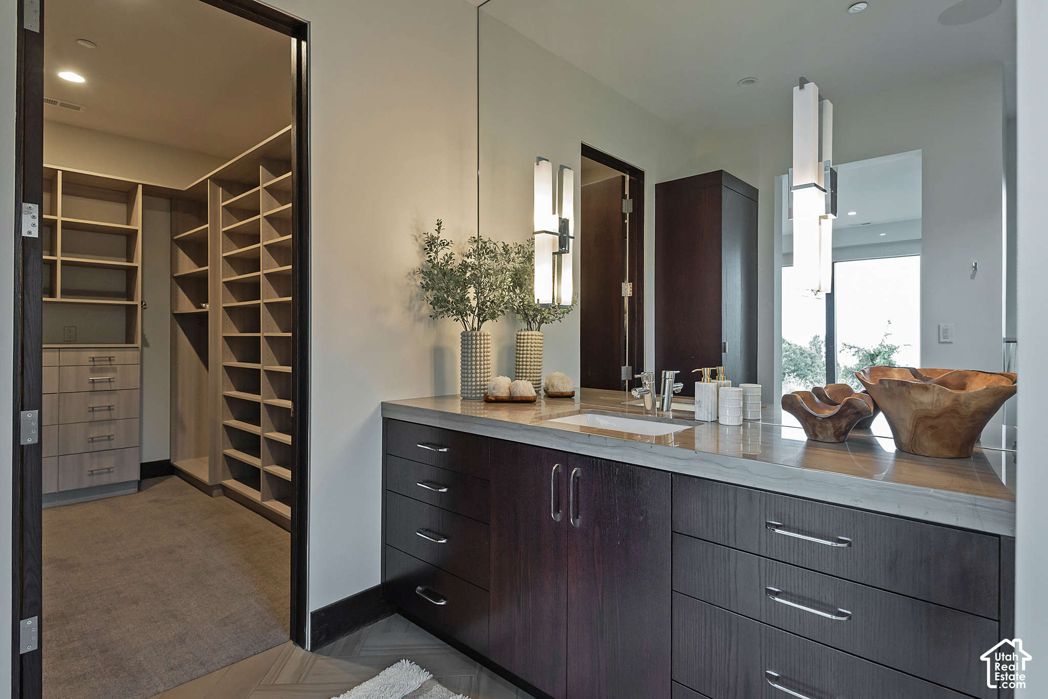 Modern bathroom vanity with dark wood cabinetry and stone counter beside a walk-in closet.