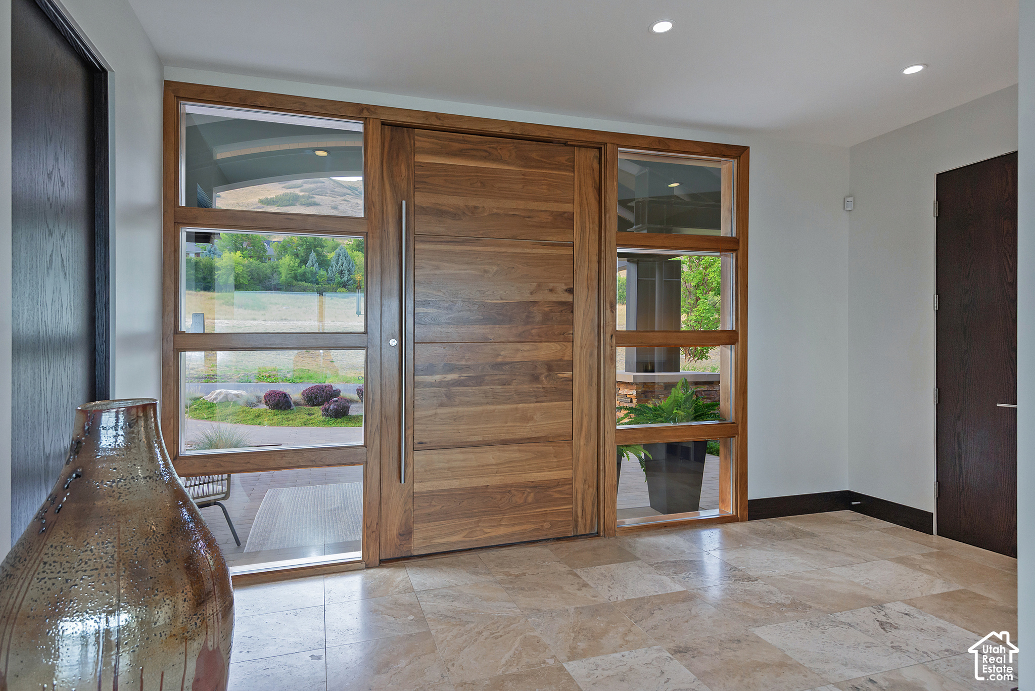 Entry foyer with a wide wood front door, tall windows, stone tile floor, and a large ceramic vase.