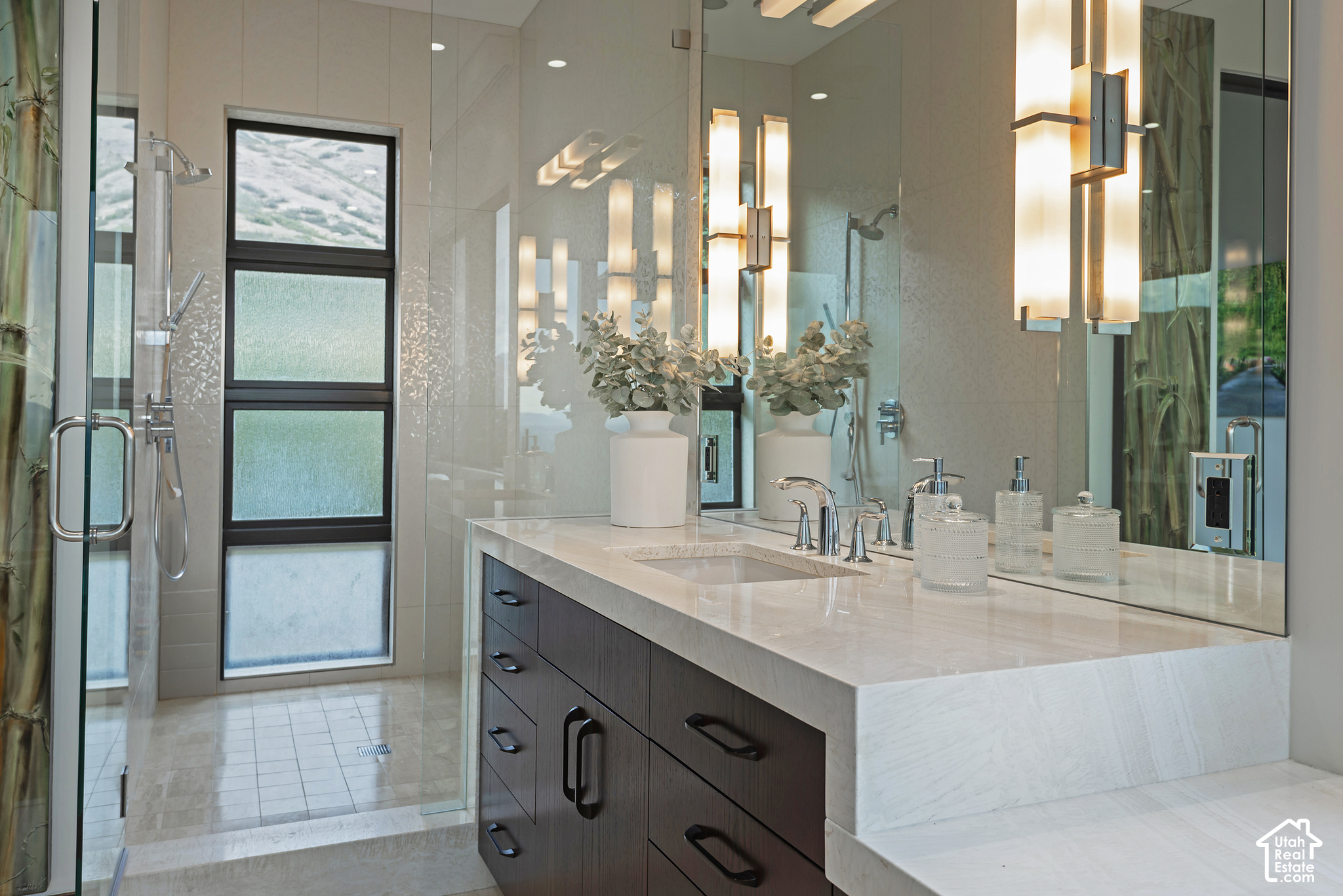 Modern bathroom with a marble vanity, dark cabinetry, glass shower, and frosted window.