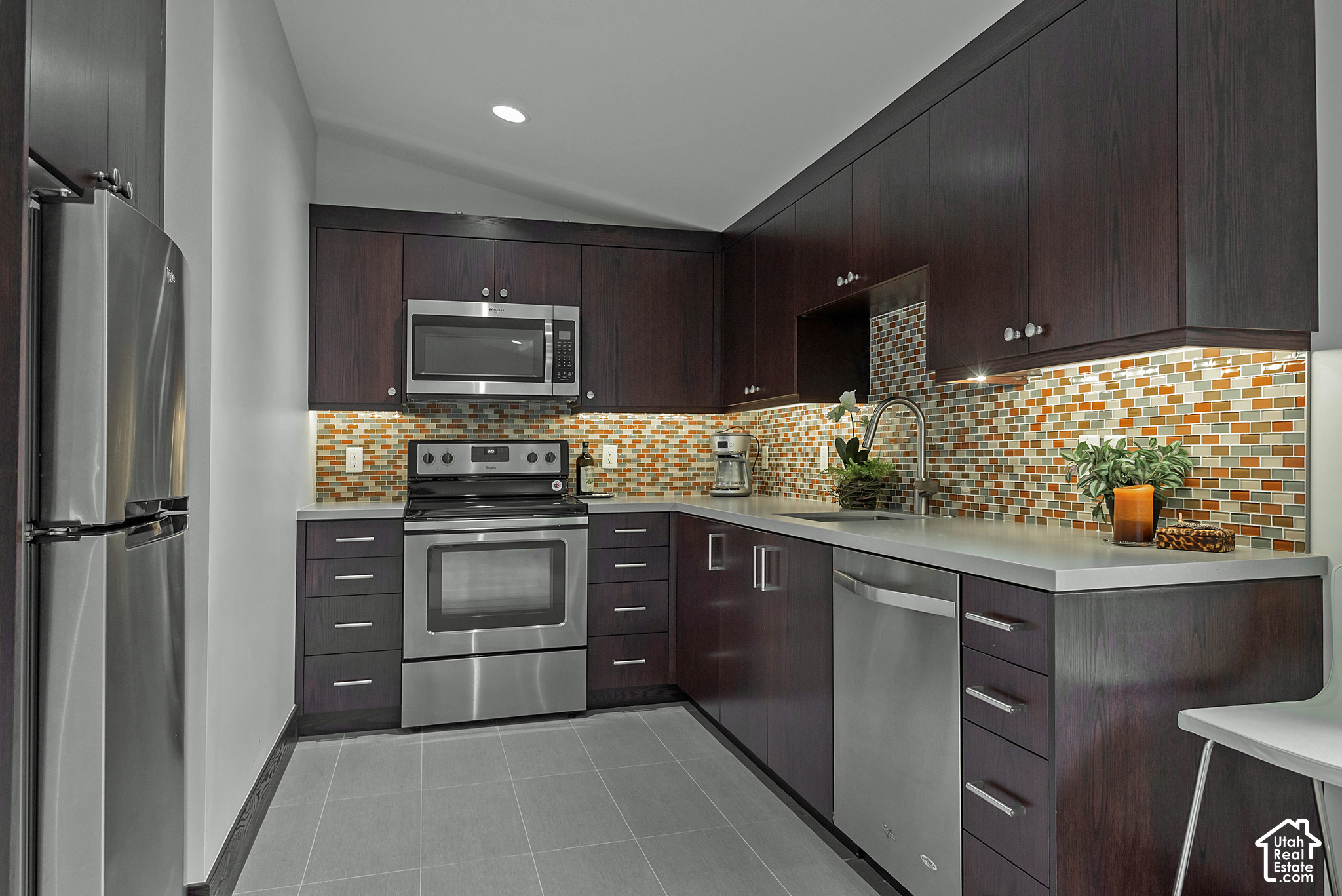 Modern kitchen with dark cabinets, stainless steel appliances, and a colorful mosaic backsplash.