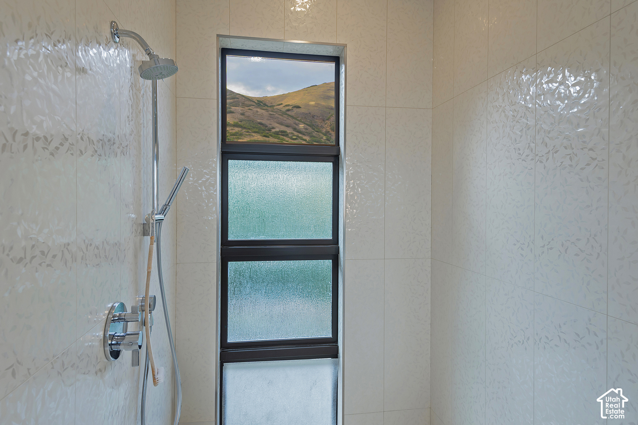 Tiled shower with chrome fixtures and a tall window framing a rolling hillside.