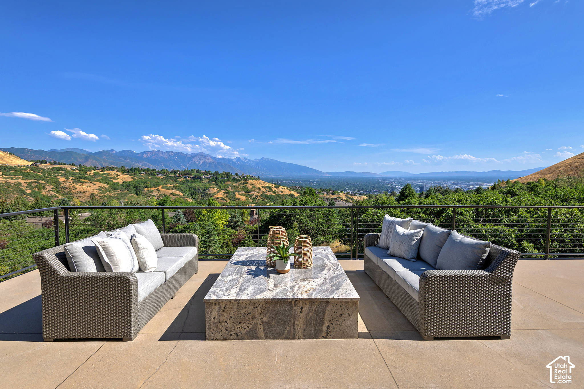 Furnished patio with woven sofas and a stone table overlooking a valley and mountain range.