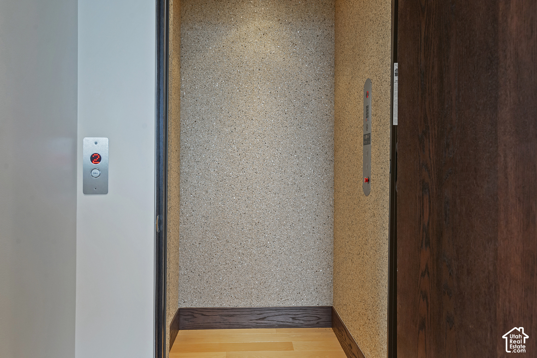 Elevator lobby with an open elevator, red floor display, textured walls, and light wood flooring.