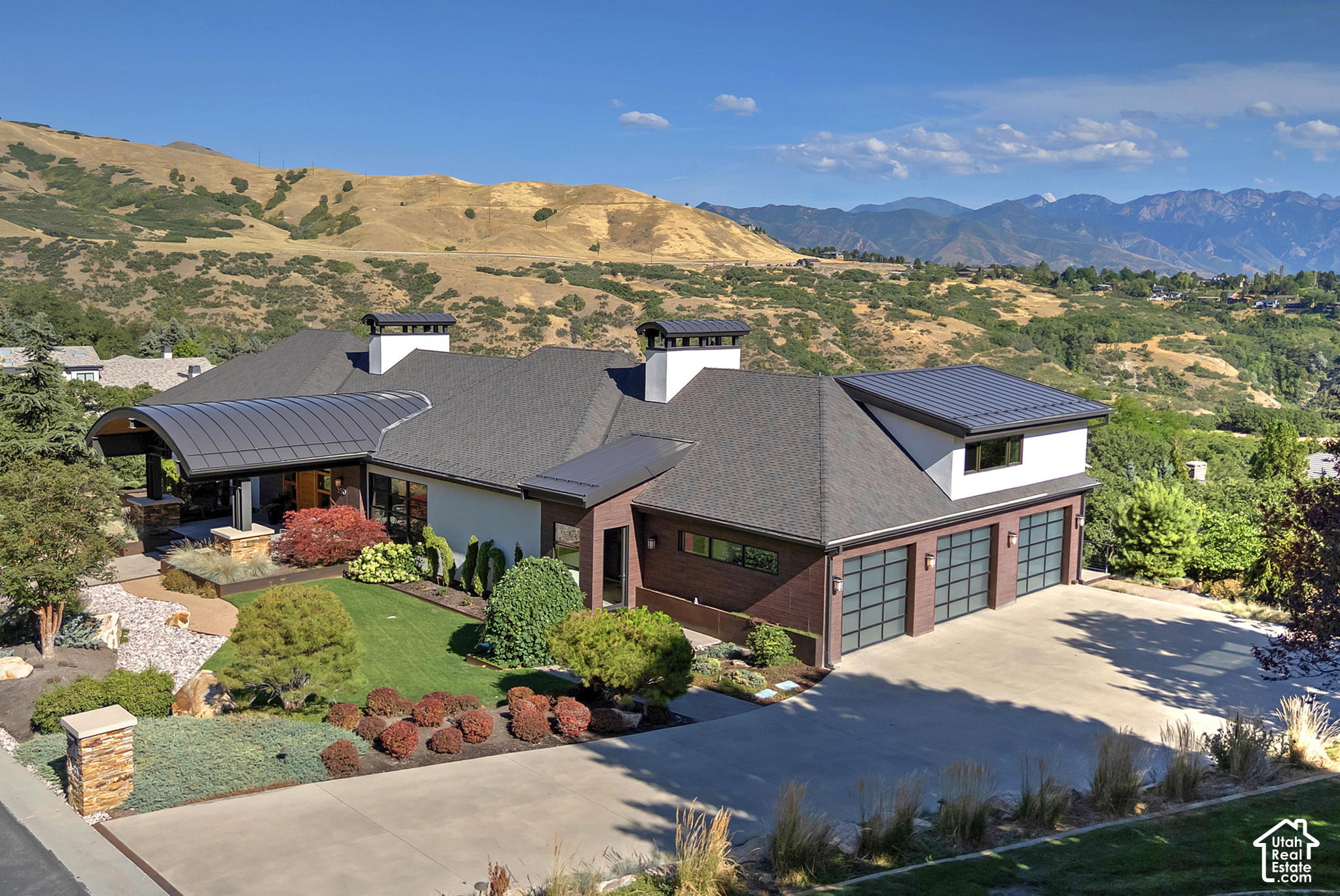 Modern home with landscaped grounds and a broad driveway, backed by dry hills and mountains.