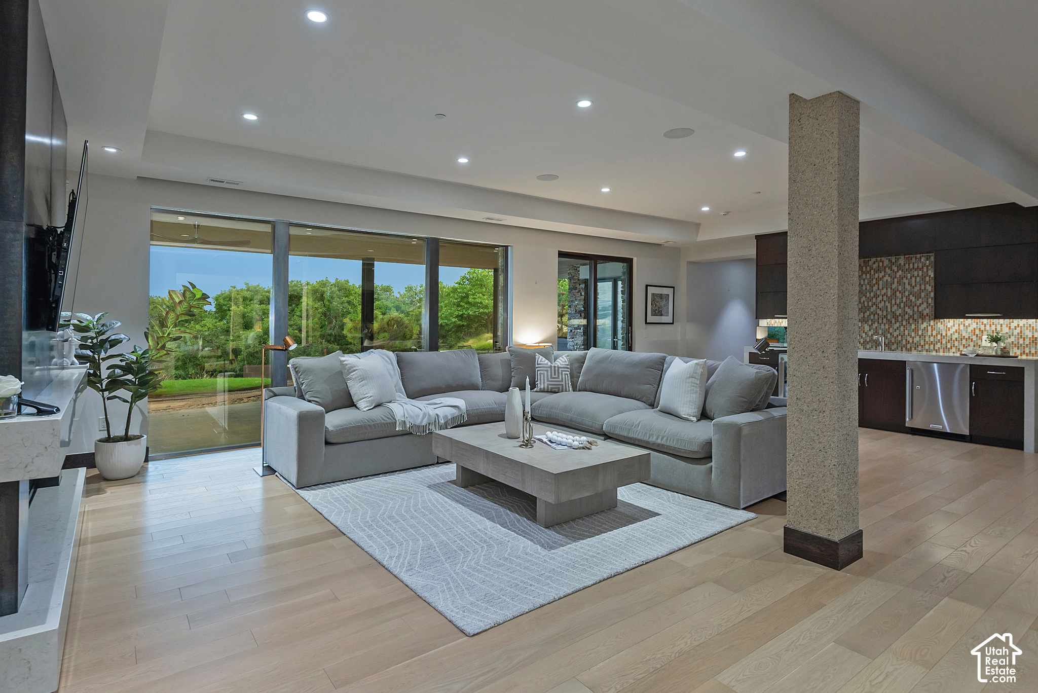 Modern living room with a gray sectional and floor-to-ceiling doors overlooking a garden.