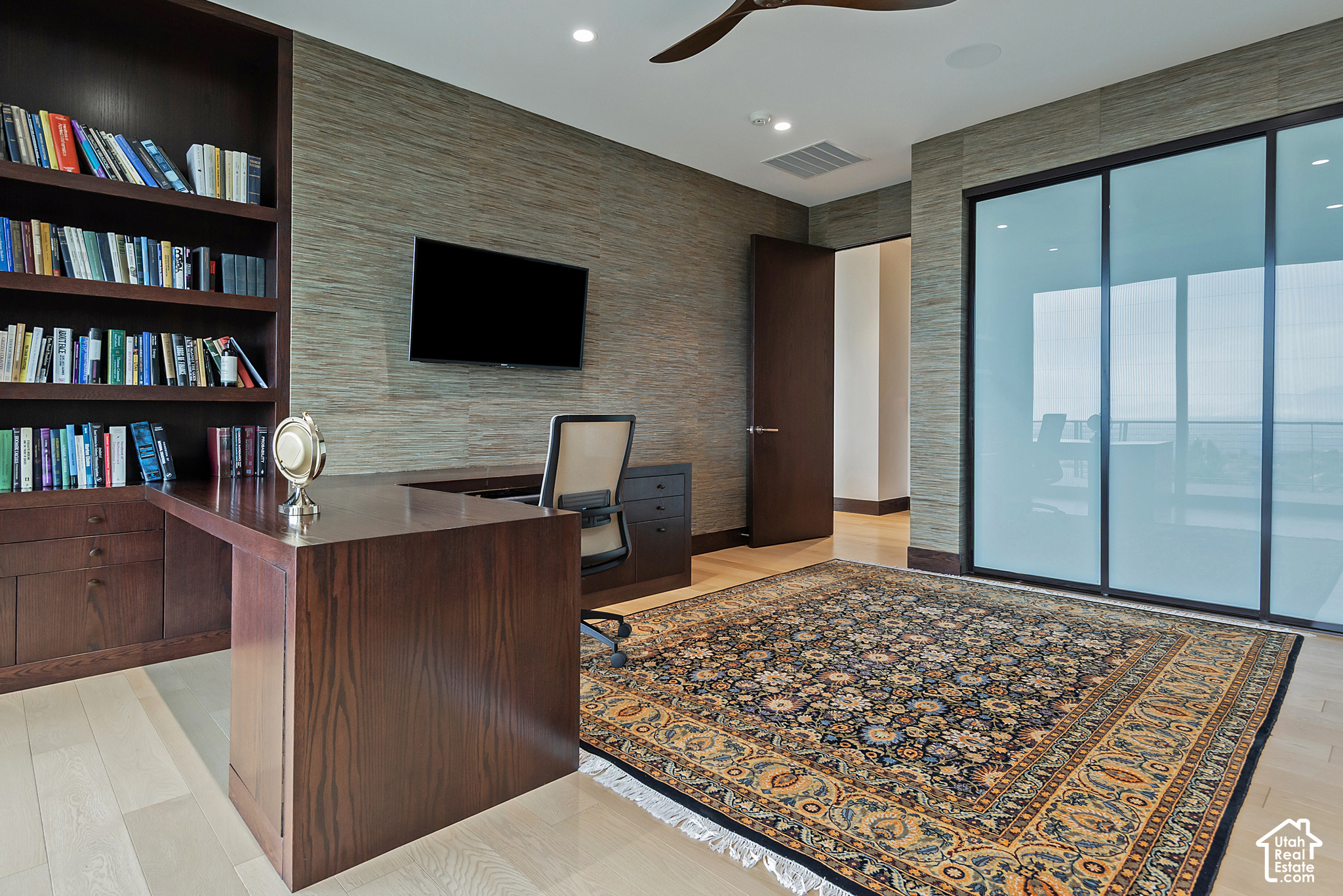 Home office with built-in bookshelves, a dark wood desk, patterned rug, and large sliding glass doors.