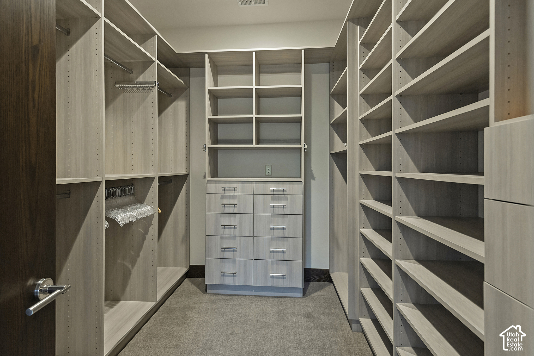 Walk-in closet with built-in shelving, hanging rods, and central drawers.