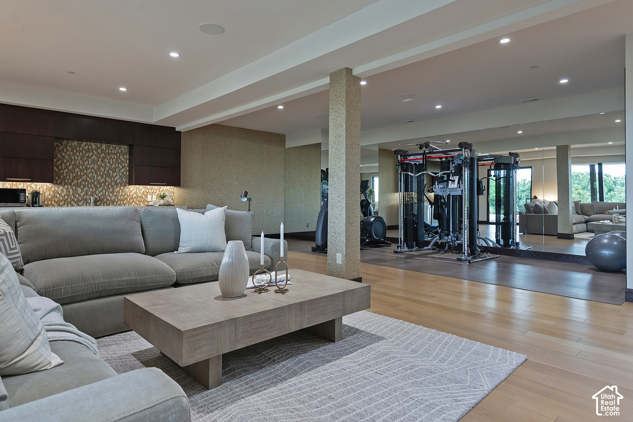 Living room with a gray sectional and coffee table beside a mirrored home gym.