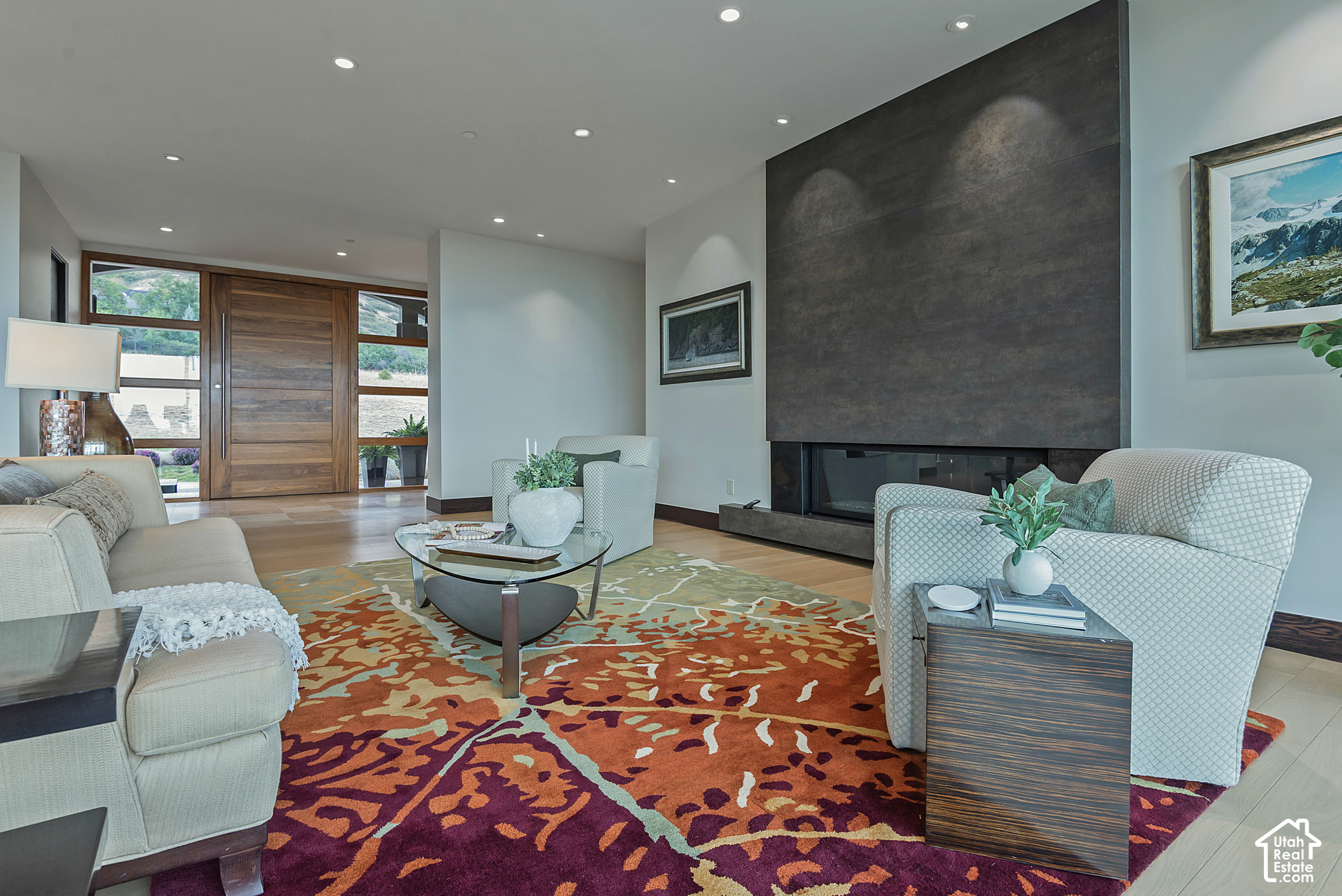 Living room with a floor-to-ceiling dark fireplace, broad wood entry door, and colorful patterned rug.