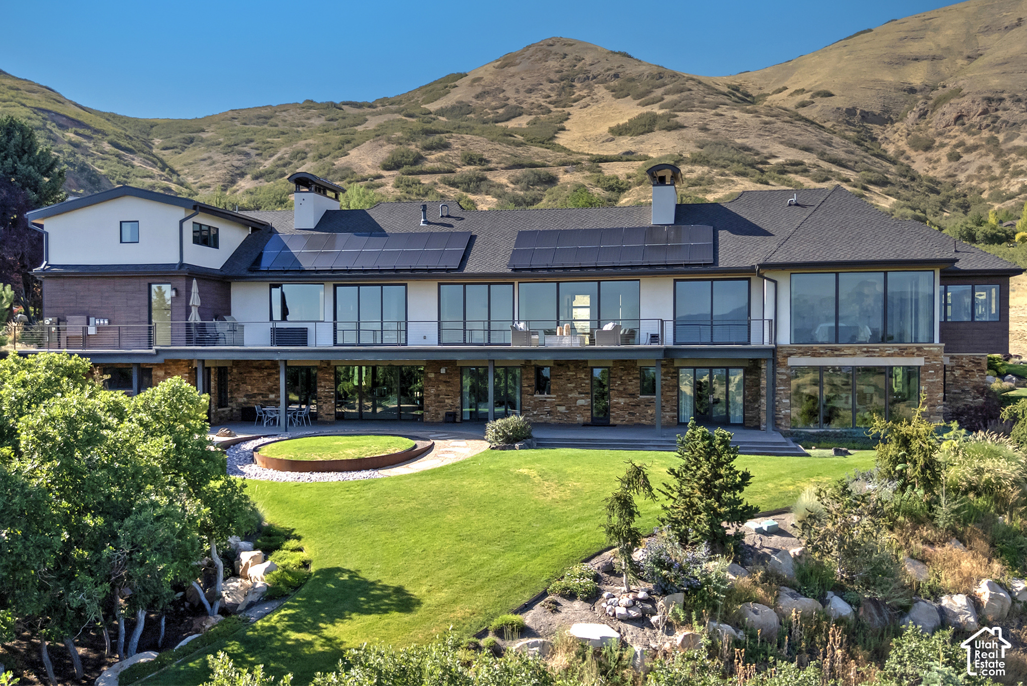 Modern multi-level home with rooftop solar panels, expansive lawn, and mountain backdrop.