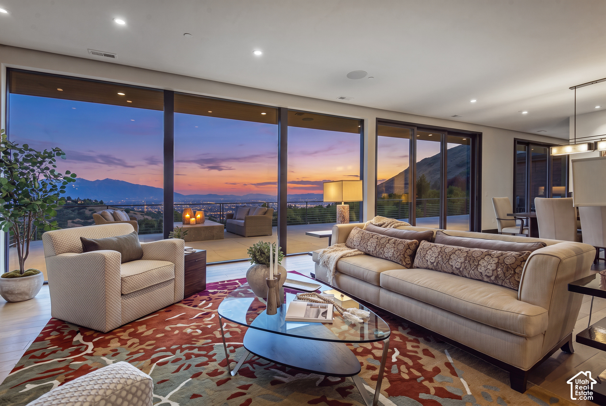 Furnished living room with expansive windows framing Salt Lake City and mountain views at sunset.