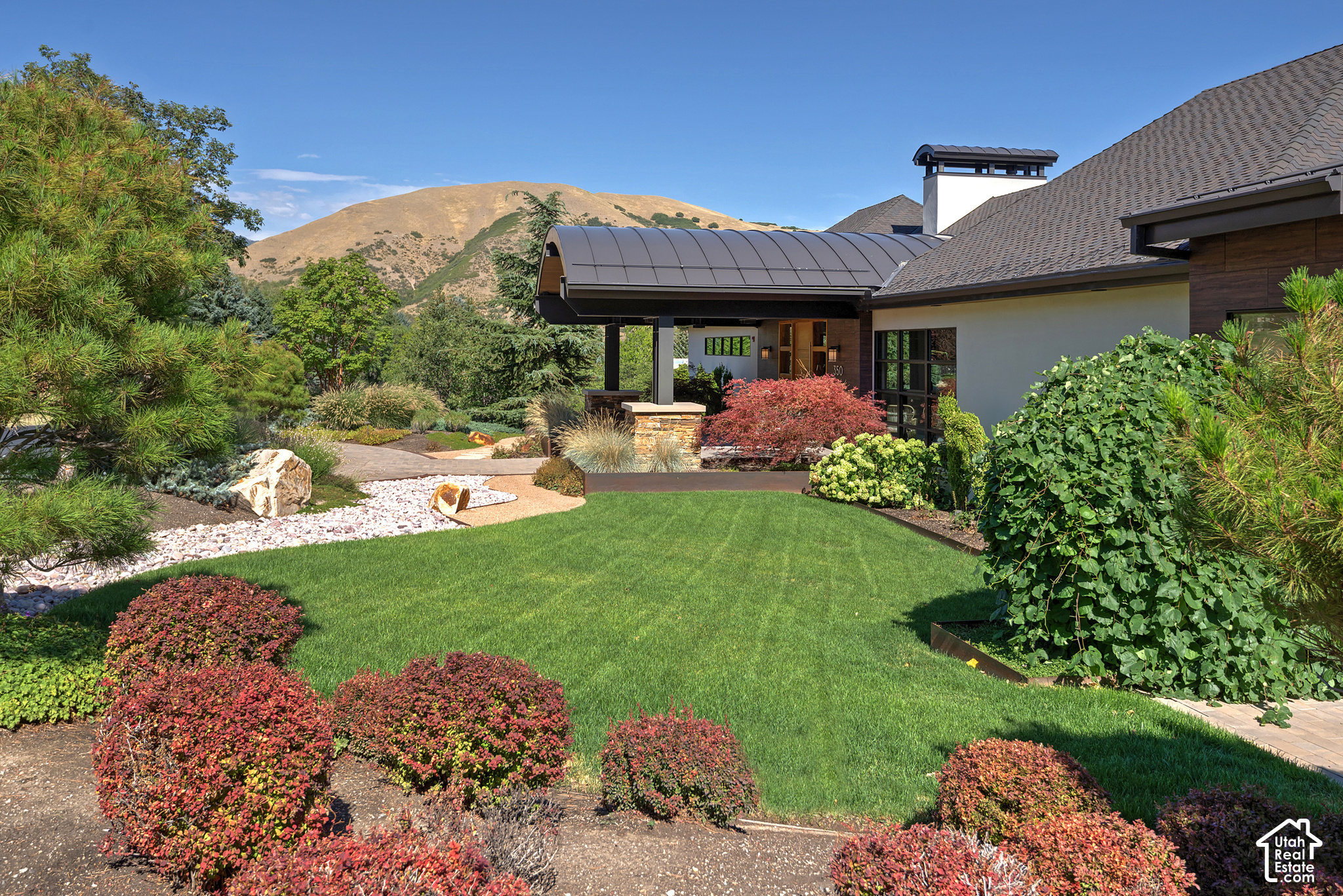 Modern home with a curved covered entry, landscaped garden, and mountain backdrop.