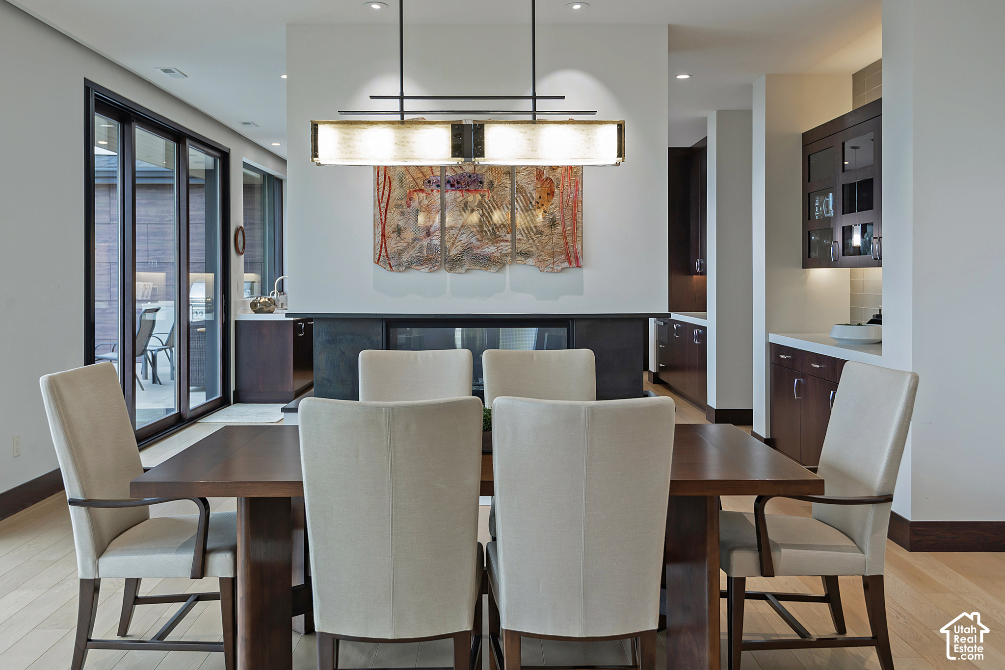 Modern dining room with a dark wood table, cream chairs, pendant light, and colorful wall art.
