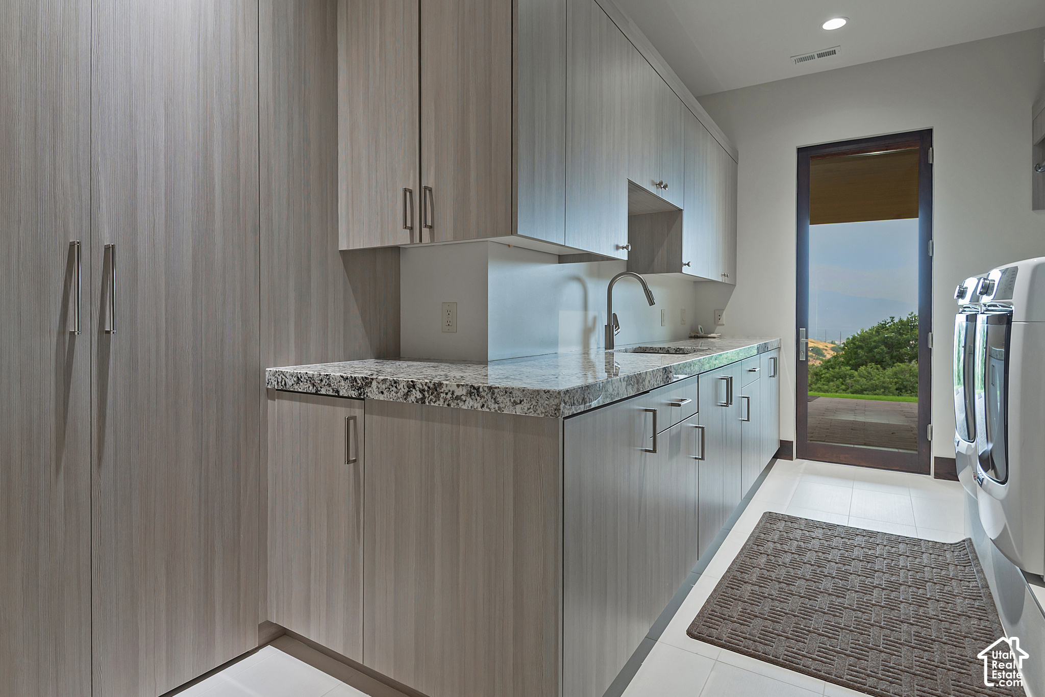 Laundry room with gray cabinetry, granite counter, washer and dryer, and a glass door to the patio.