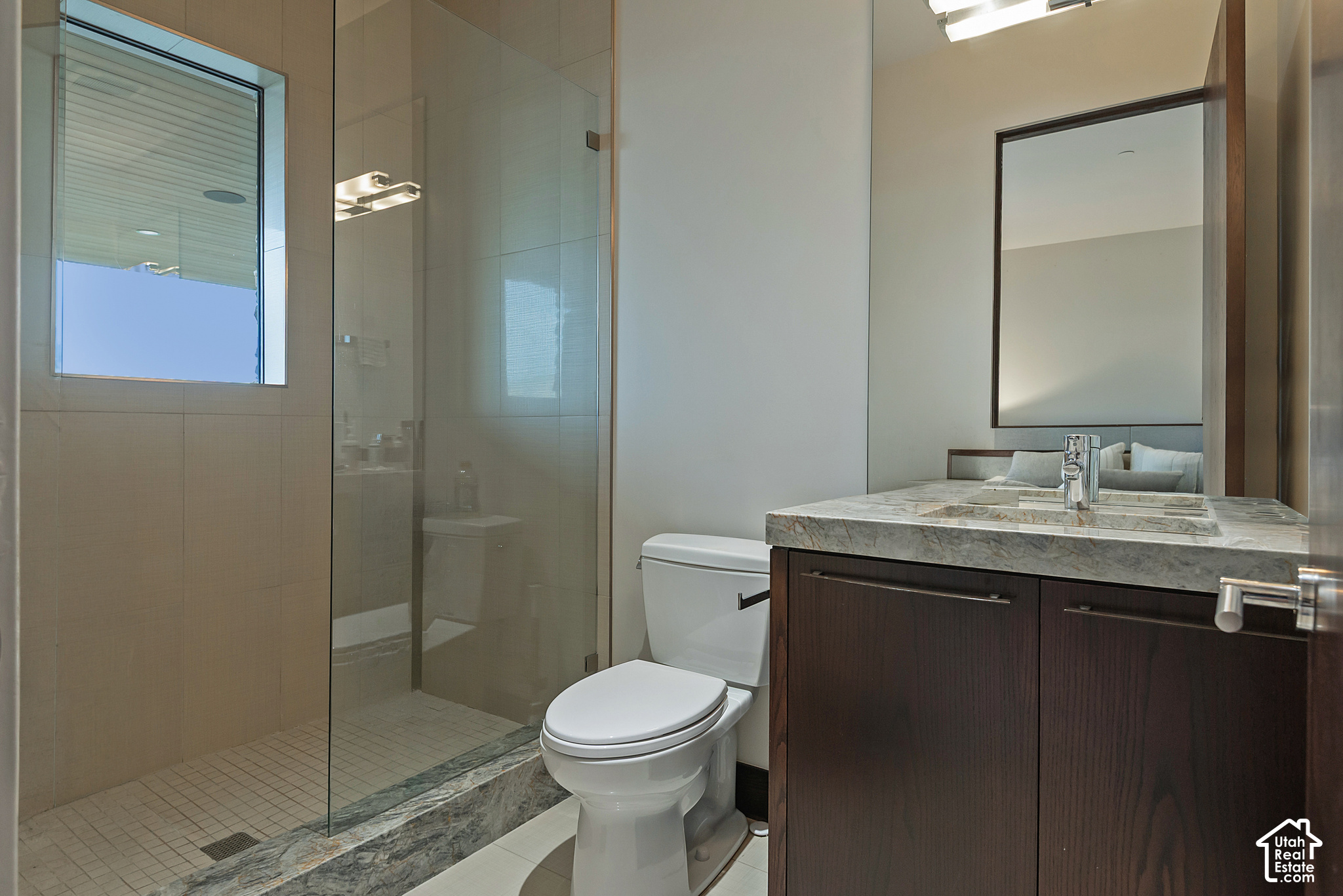 Bathroom with a glass shower, toilet, and dark wood vanity with a stone countertop.