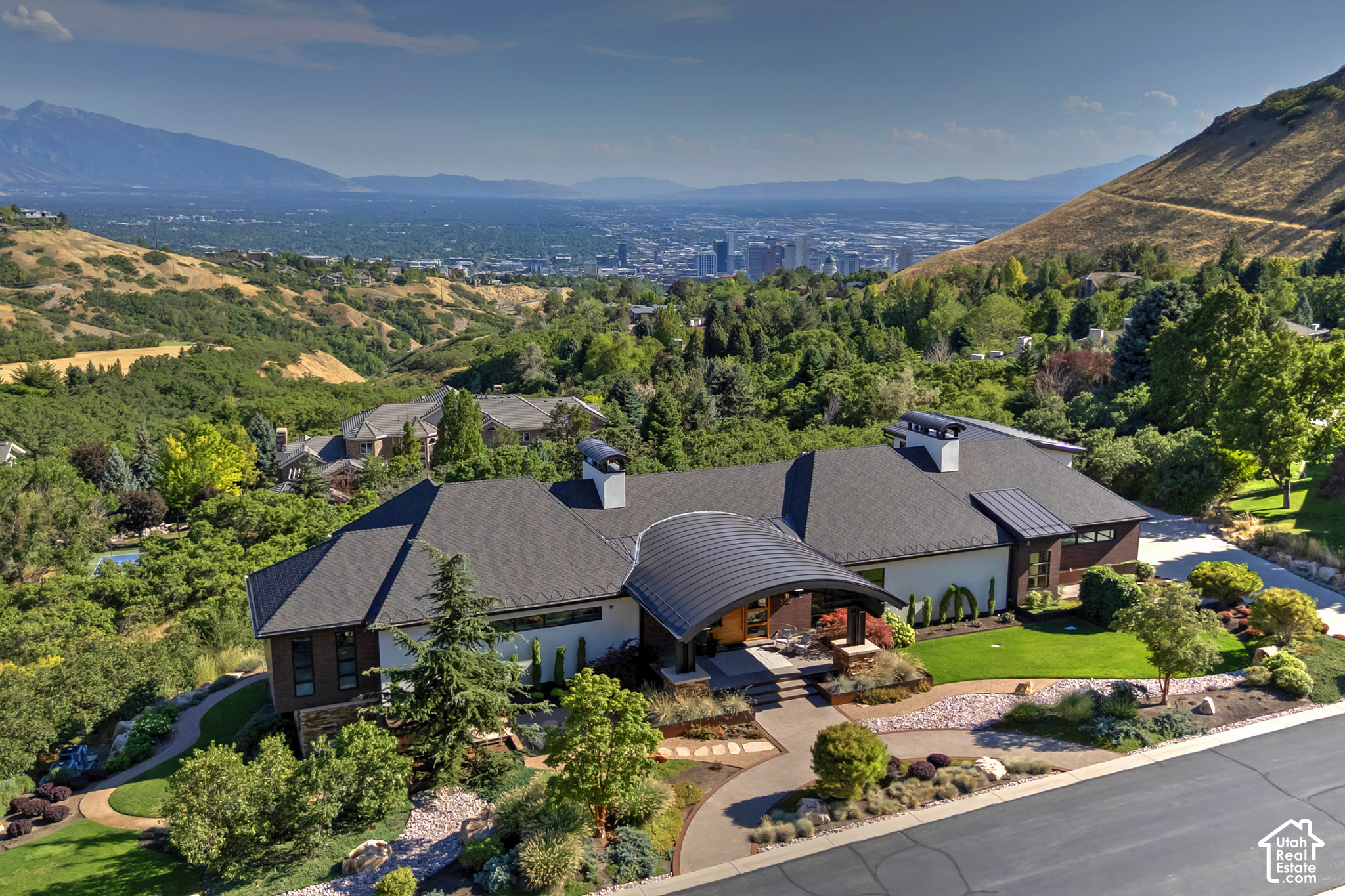 Modern hillside home with landscaped grounds, Salt Lake City skyline, and mountains beyond.