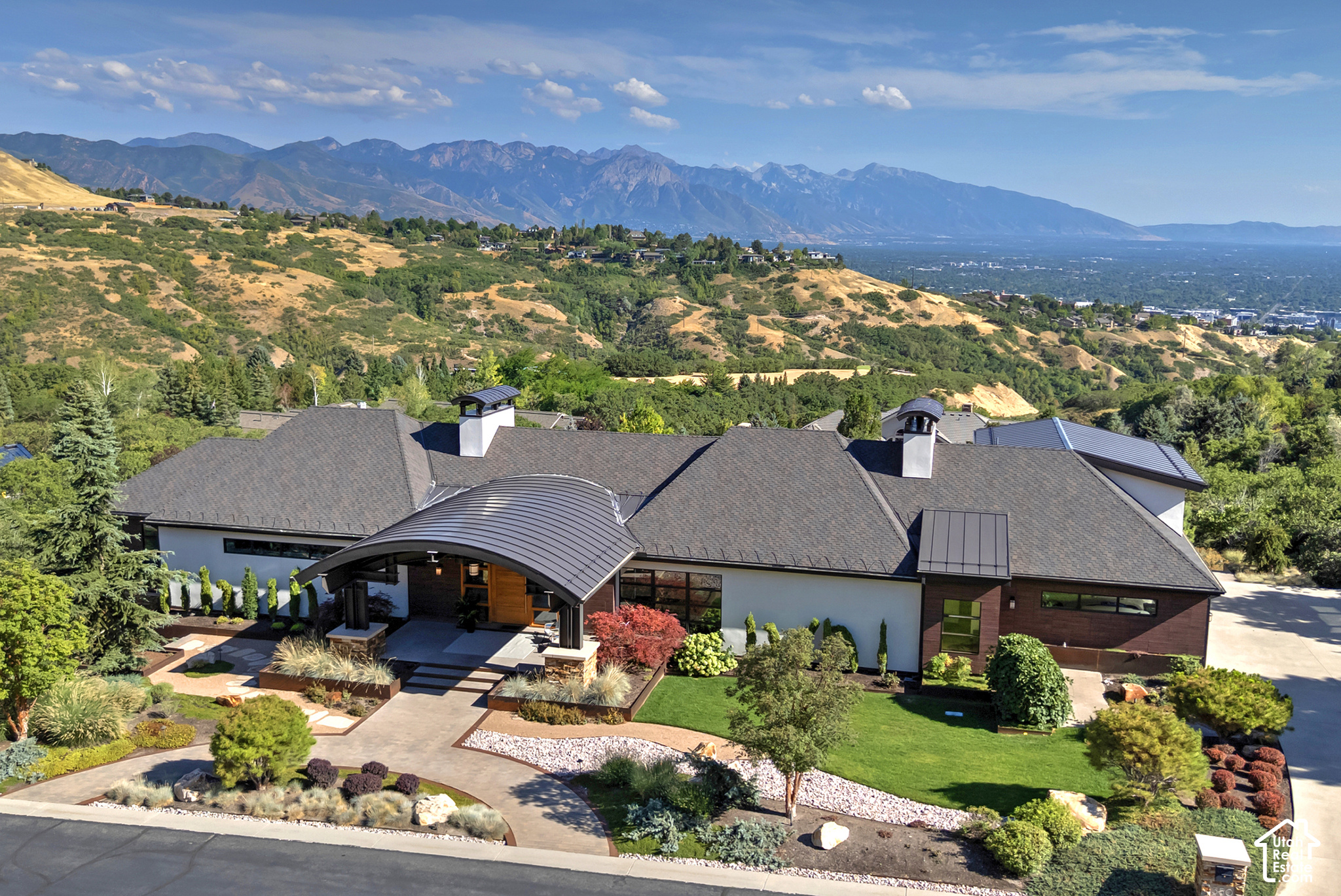 Aerial view of a modern home with landscaped grounds and mountains in the background.