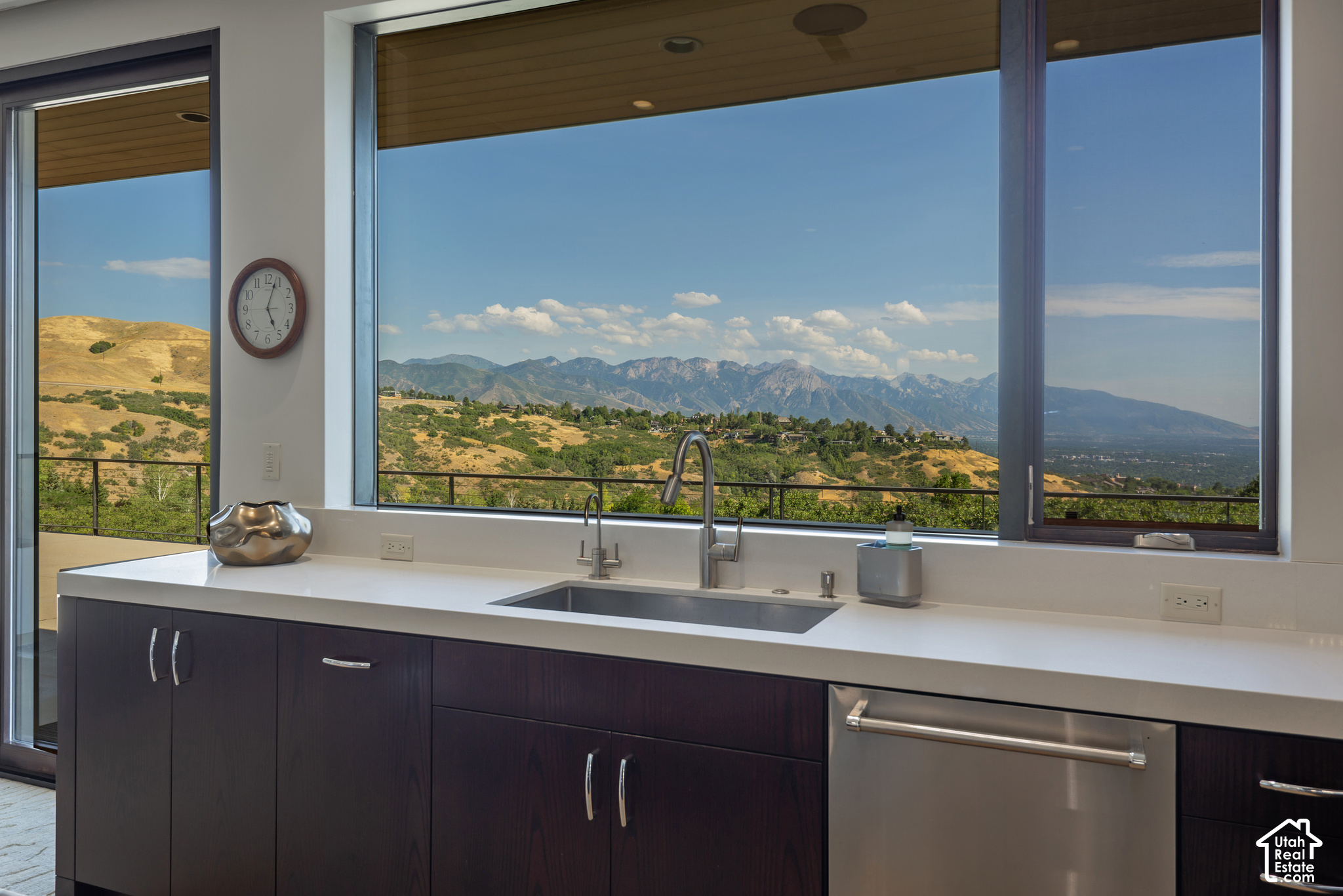 Modern kitchen sink and counter overlooking dry hills and a mountain range through large windows.