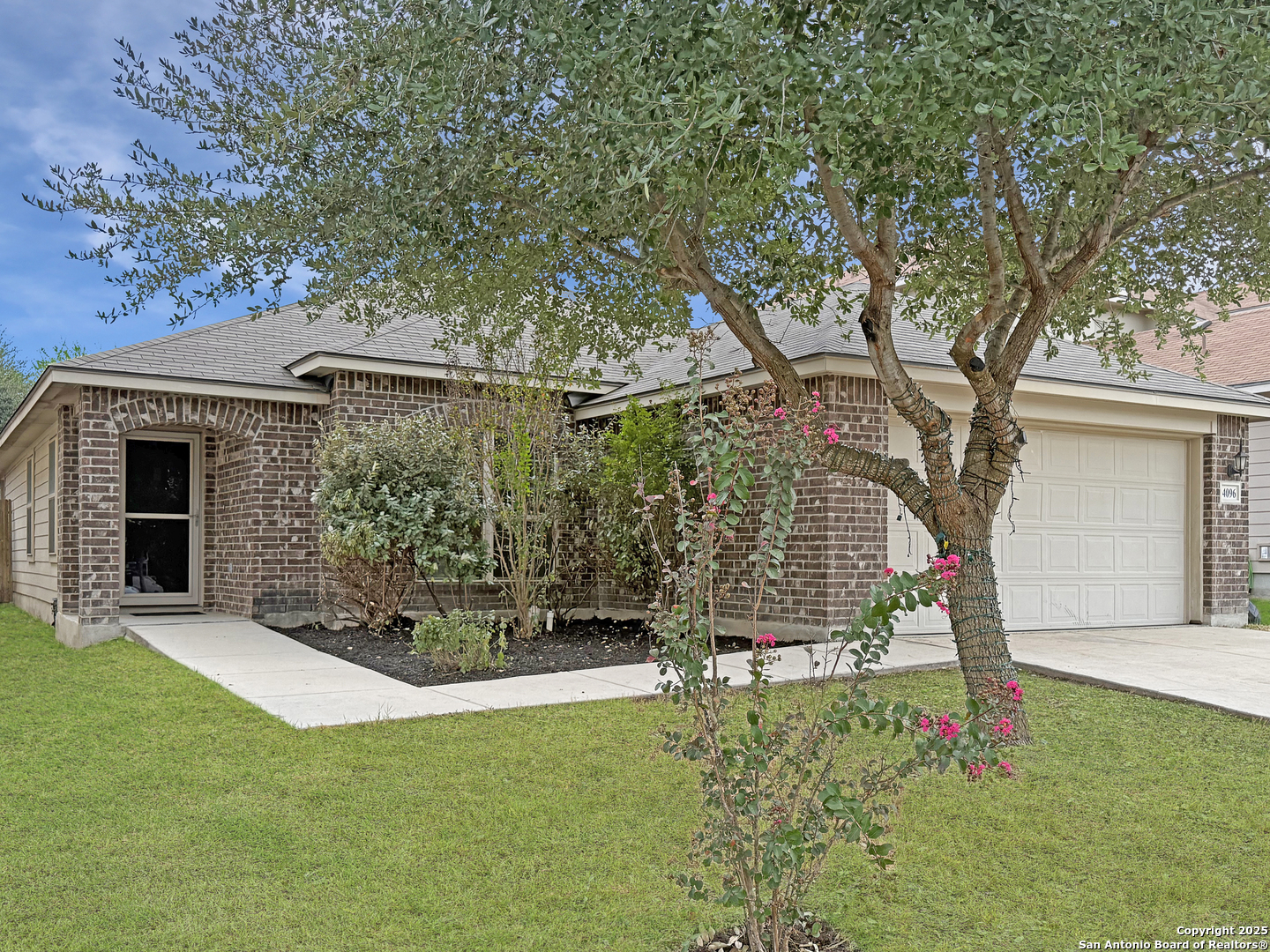Single-story brick house with a white garage door, shaded by a large tree.