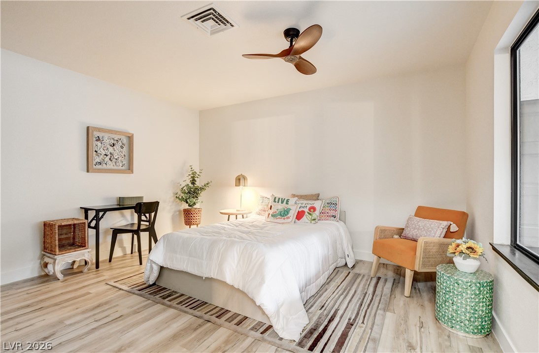 Staged bedroom with a white bed, striped rug, small desk, and orange armchair beside a large window.