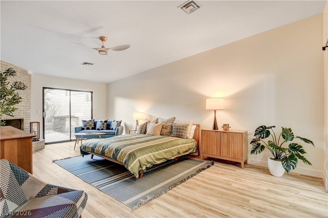 Staged bedroom with green striped bedding, a blue loveseat, sliding glass doors, and a brick fireplace.