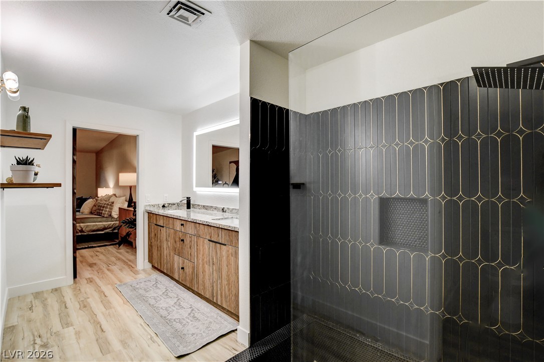 Modern bathroom with a black-and-gold tiled shower and wood-finish vanity.