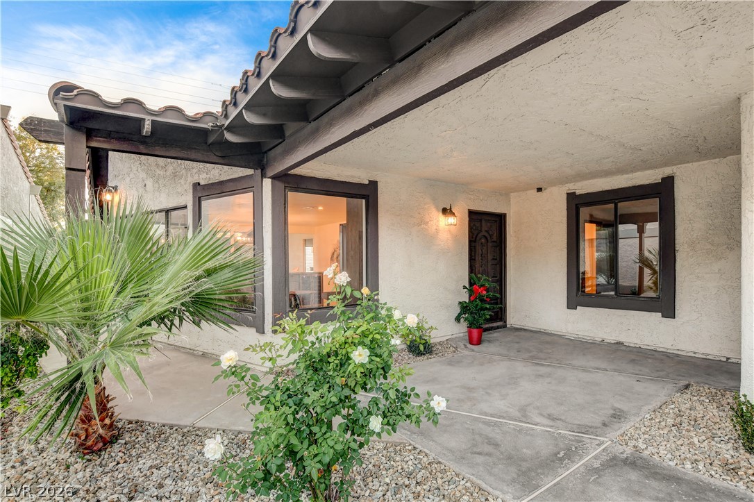Covered front entry with dark-trimmed windows, a decorative door, and flowering plants.