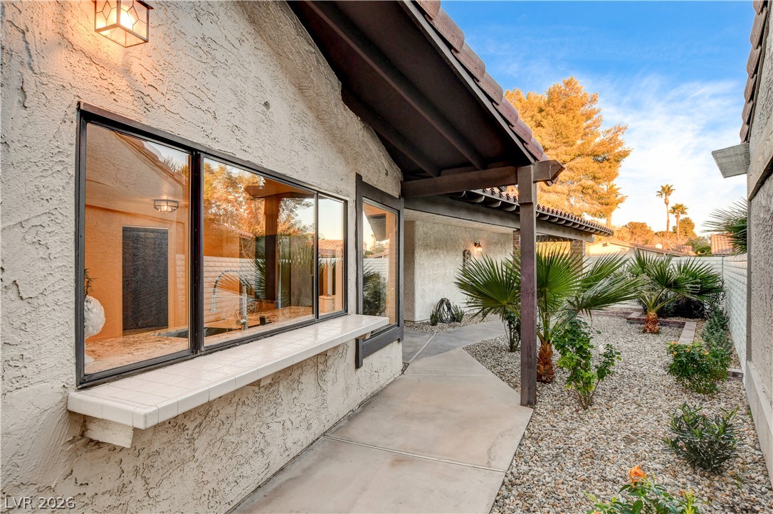 Home courtyard with a covered walkway, large windows, gravel landscaping, and palm trees.