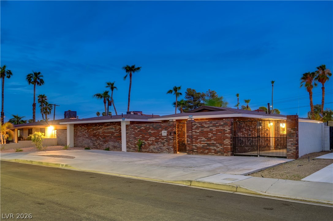 Single-story brick home with black metal gates and a broad driveway at dusk.
