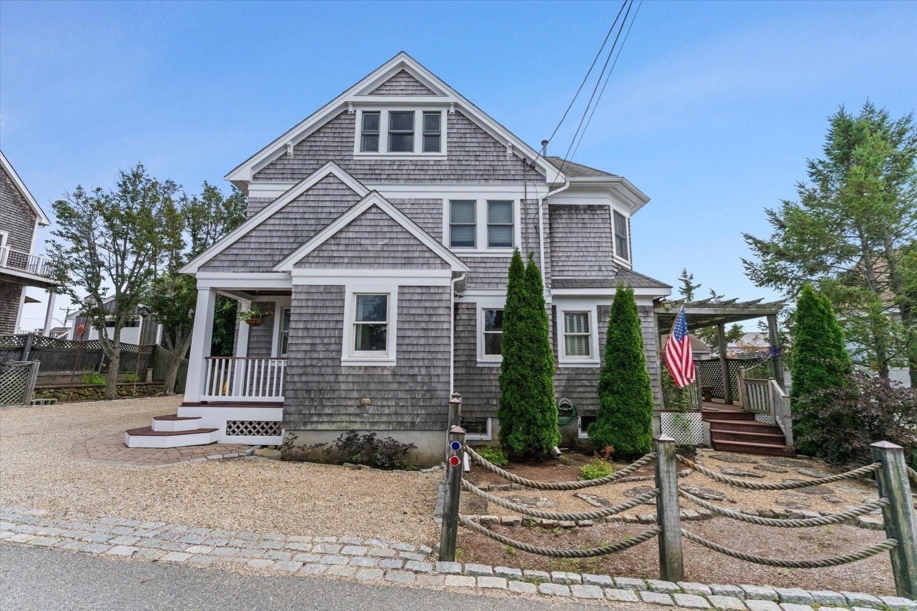 Gray shingle-sided house with multiple gables, a covered porch, and a gravel driveway.