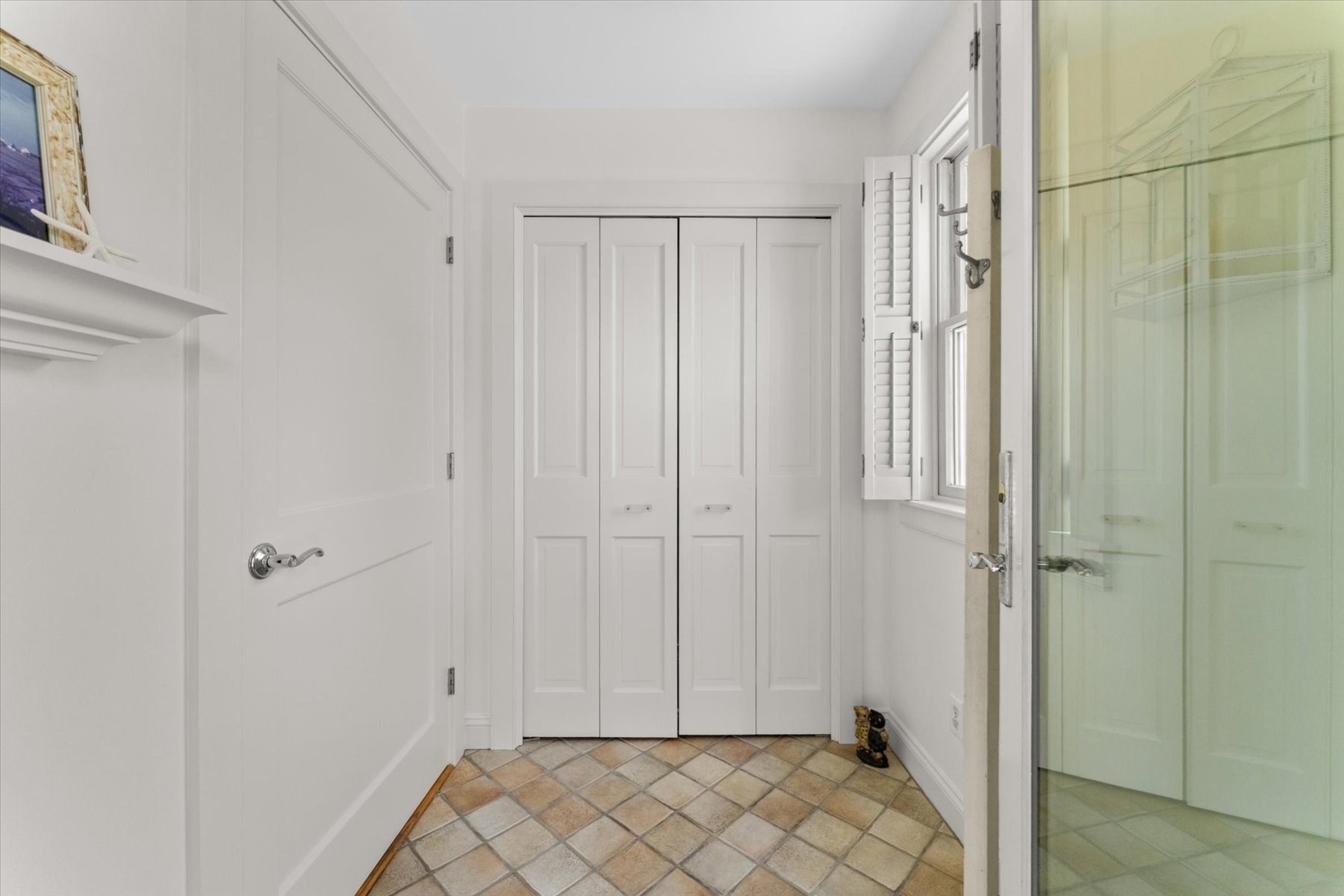 Entryway with white paneled closets, shuttered window, and patterned tile floor.