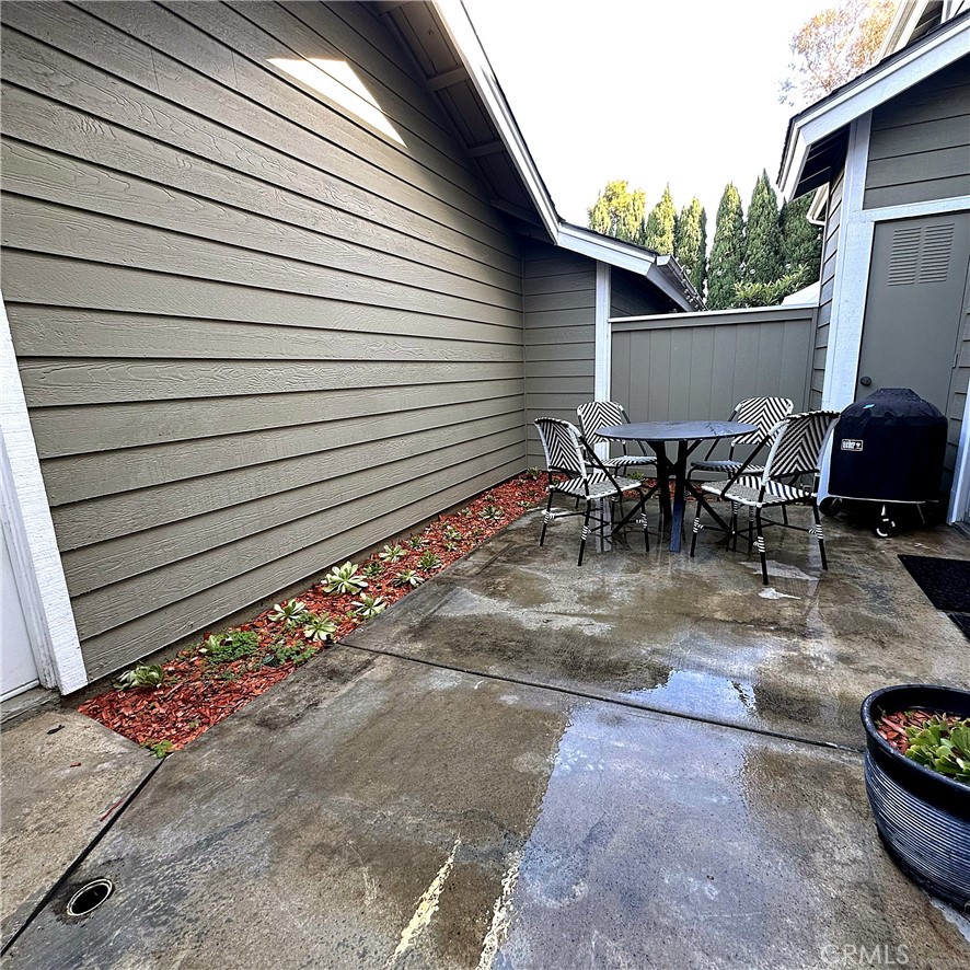 Patio with a round table, striped chairs, barbecue grill, and wet concrete.